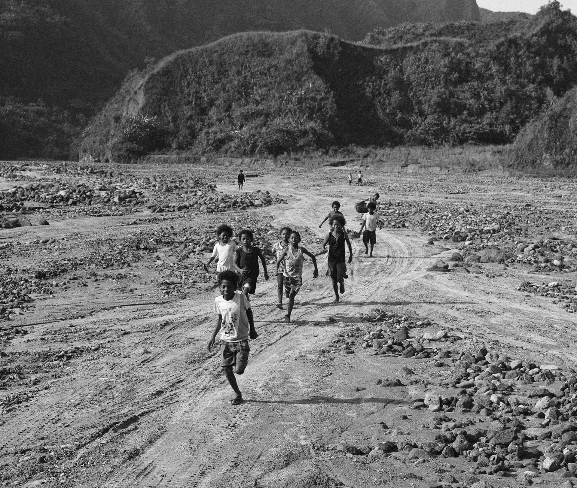 Black and white children running on rocky terrain with mountains and valley landscape