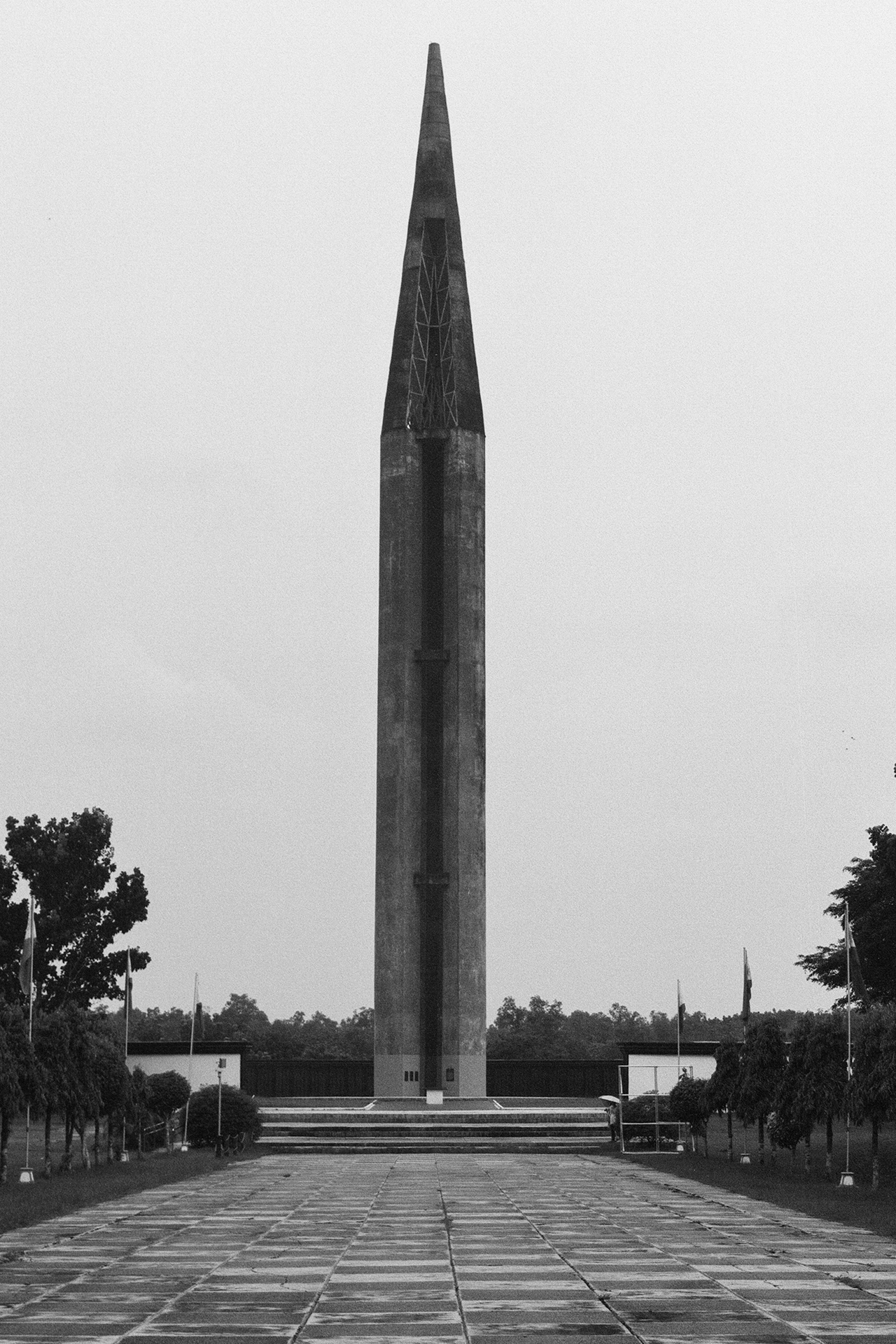 Black and white tall commemorative obelisk monument on formal plaza with tree-lined avenue