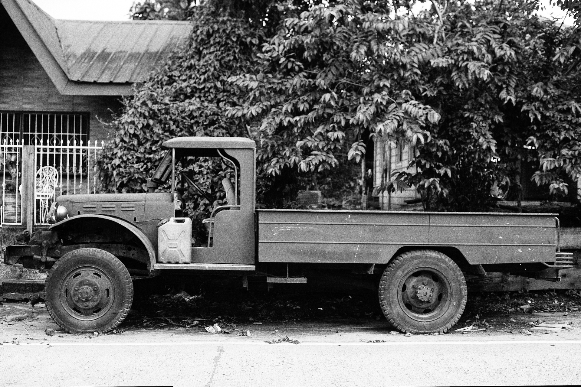 Black and white vintage truck with flat bed parked near buildings and abundant green vegetation