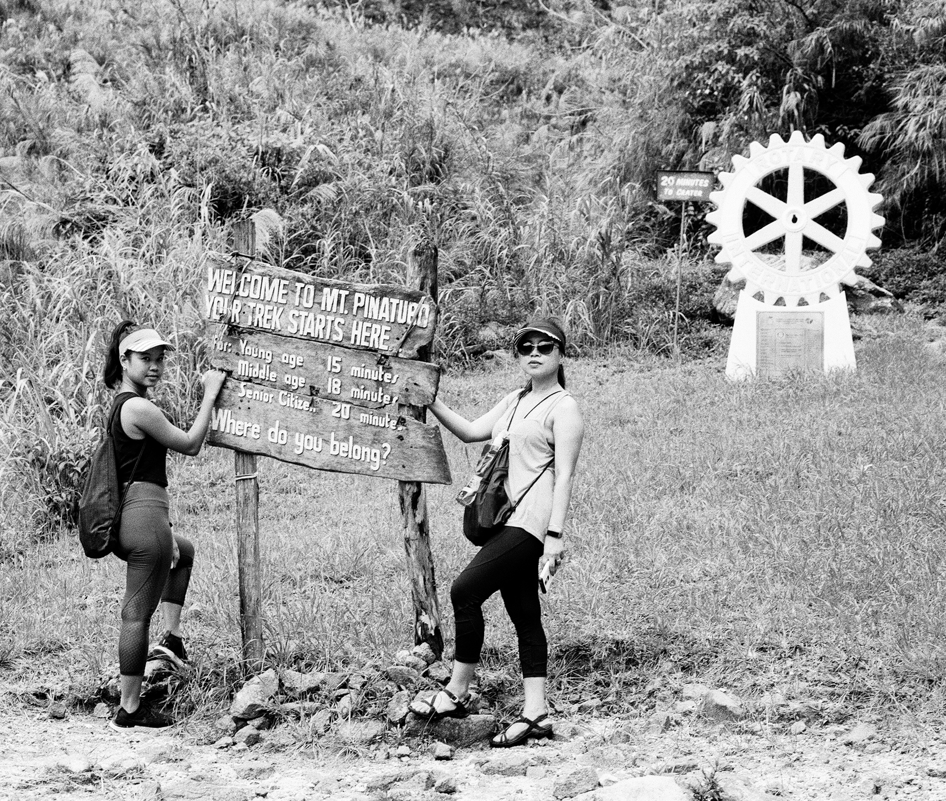 Black and white two women at Mt Pinaturo hiking sign with gear and mountains with white gear symbol