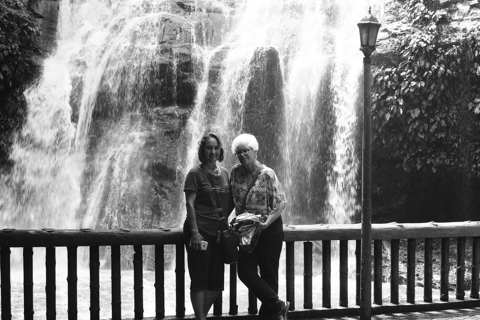 Black and white two women standing on platform at impressive waterfall curtain backdrop