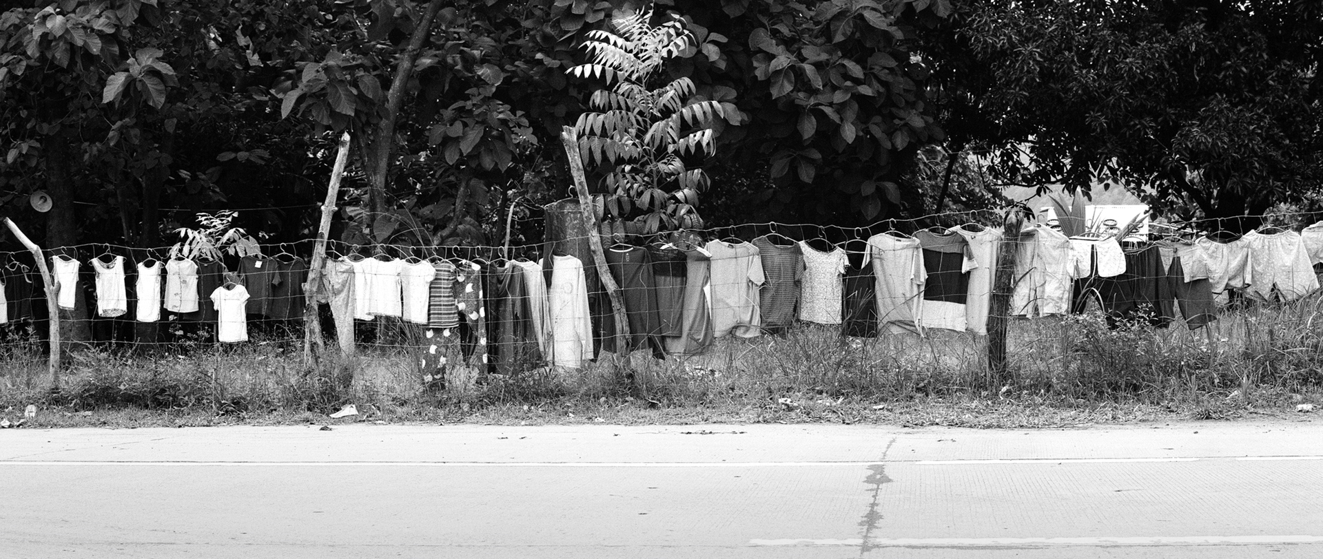 Black and white long clothesline with white and patterned laundry drying roadside with vegetation