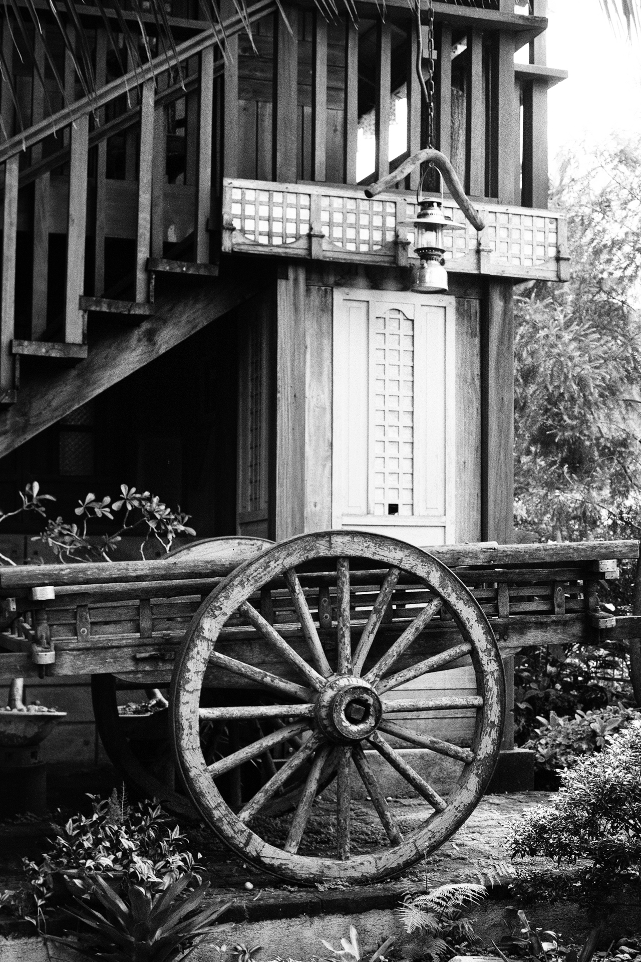 Black and white wooden wagon wheel leaning against traditional wooden stilt house architecture
