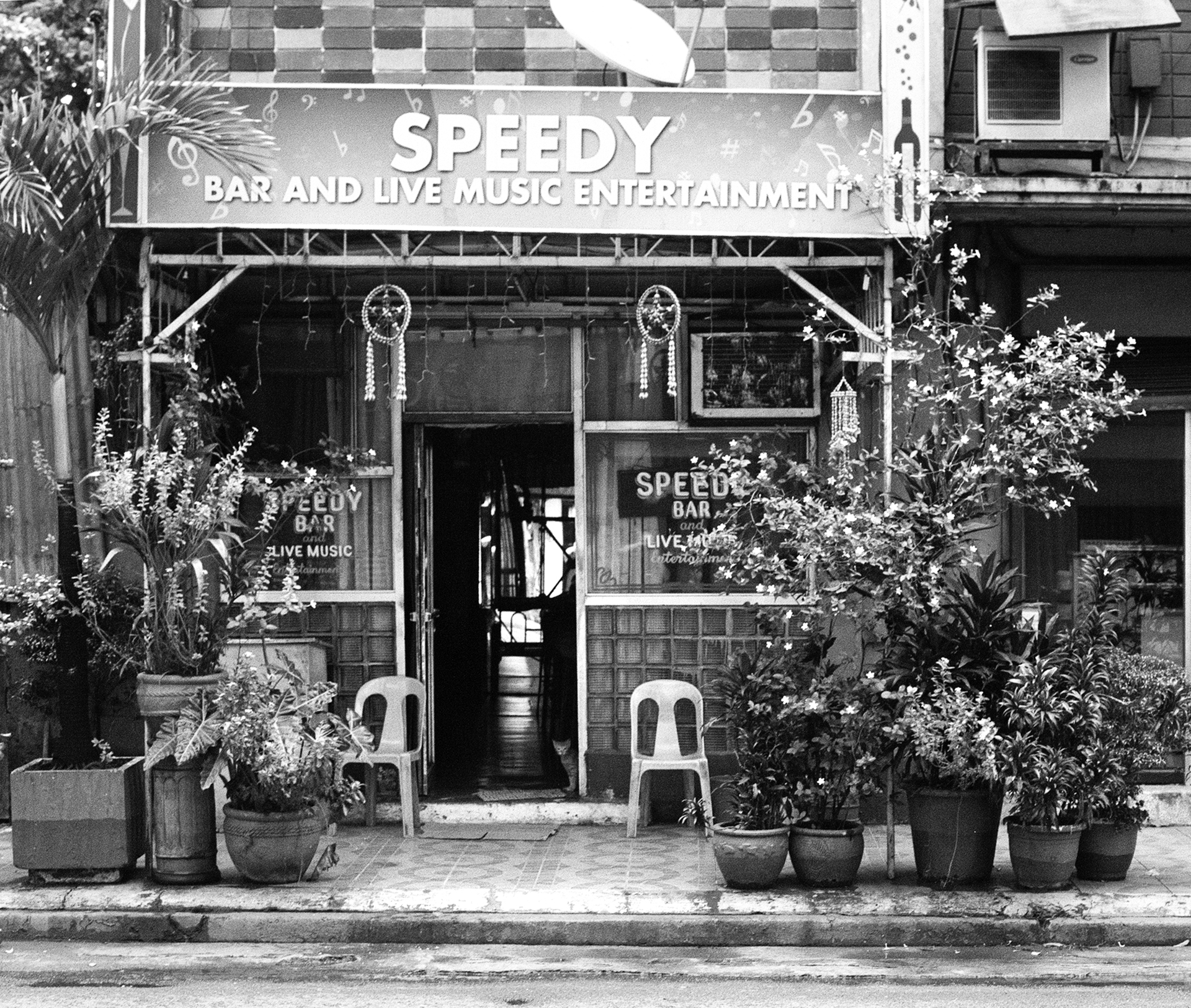 Black and white storefront of Speedy Bar and Live Music Entertainment with decorative plants seating