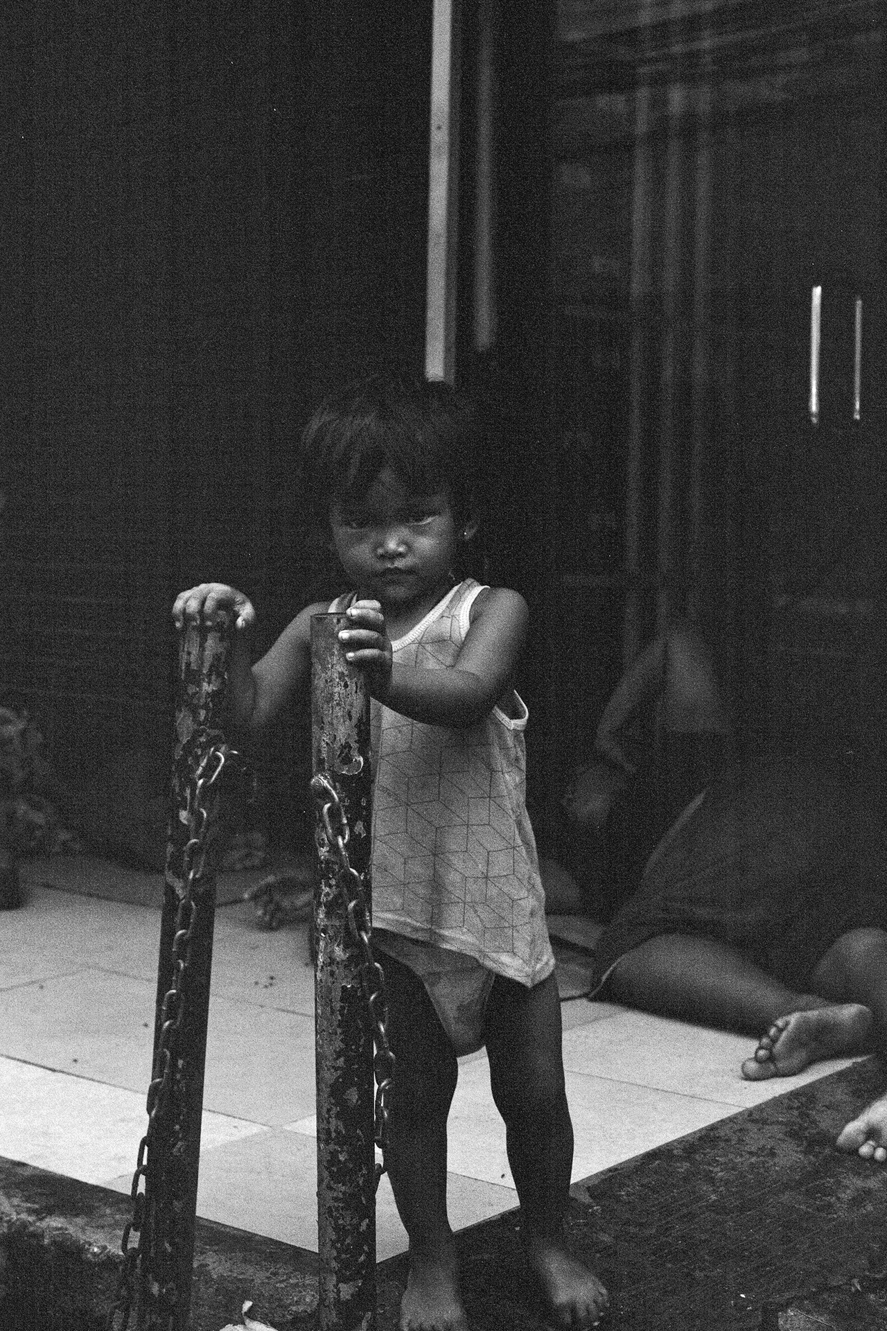 Black and white young child holding chain links in dark sheltered indoor space at night