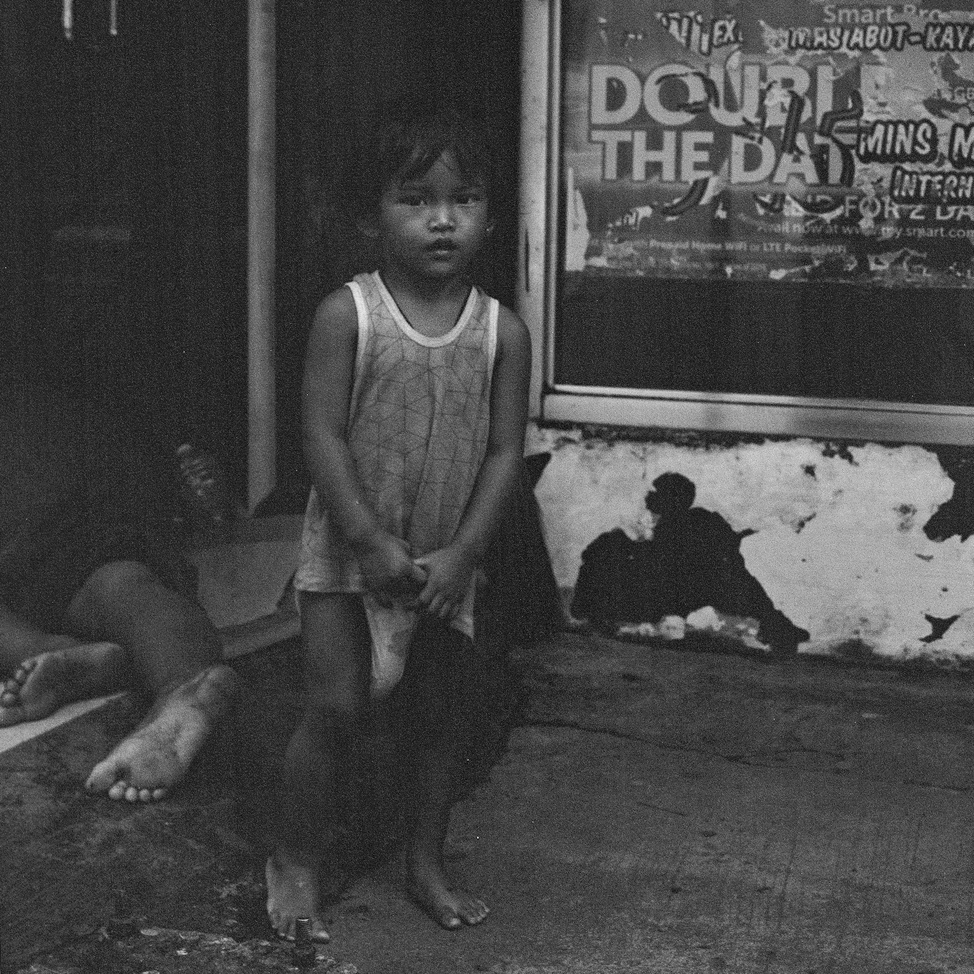 Black and white portrait of standing child in white tank top inside dark indoor structure