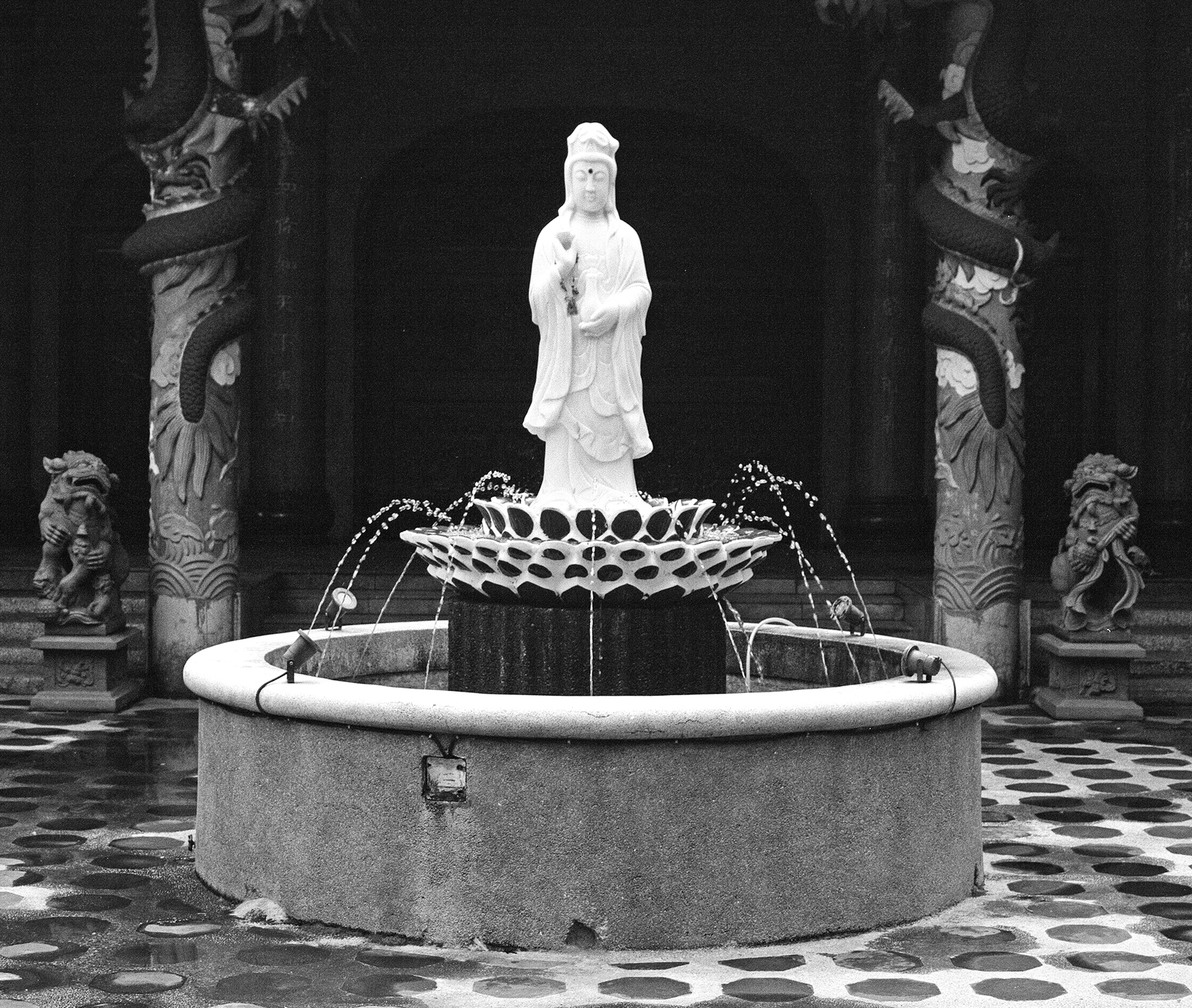 Black and white white religious statue on ornate fountain with carved dragon supports and temple backdrop