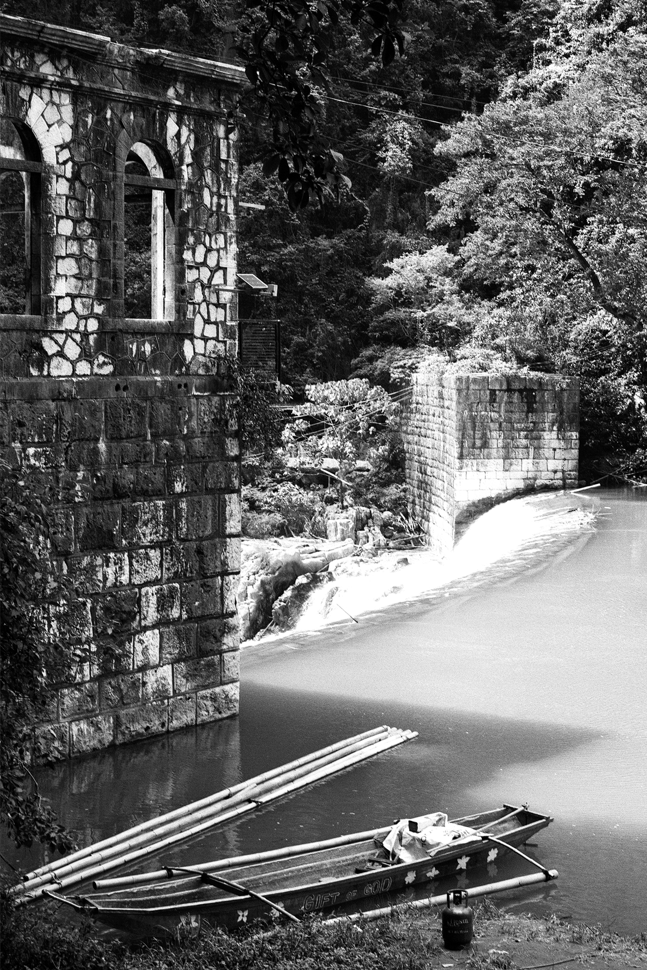 Black and white stone arched gateway with water channel and traditional wooden boat moored foreground