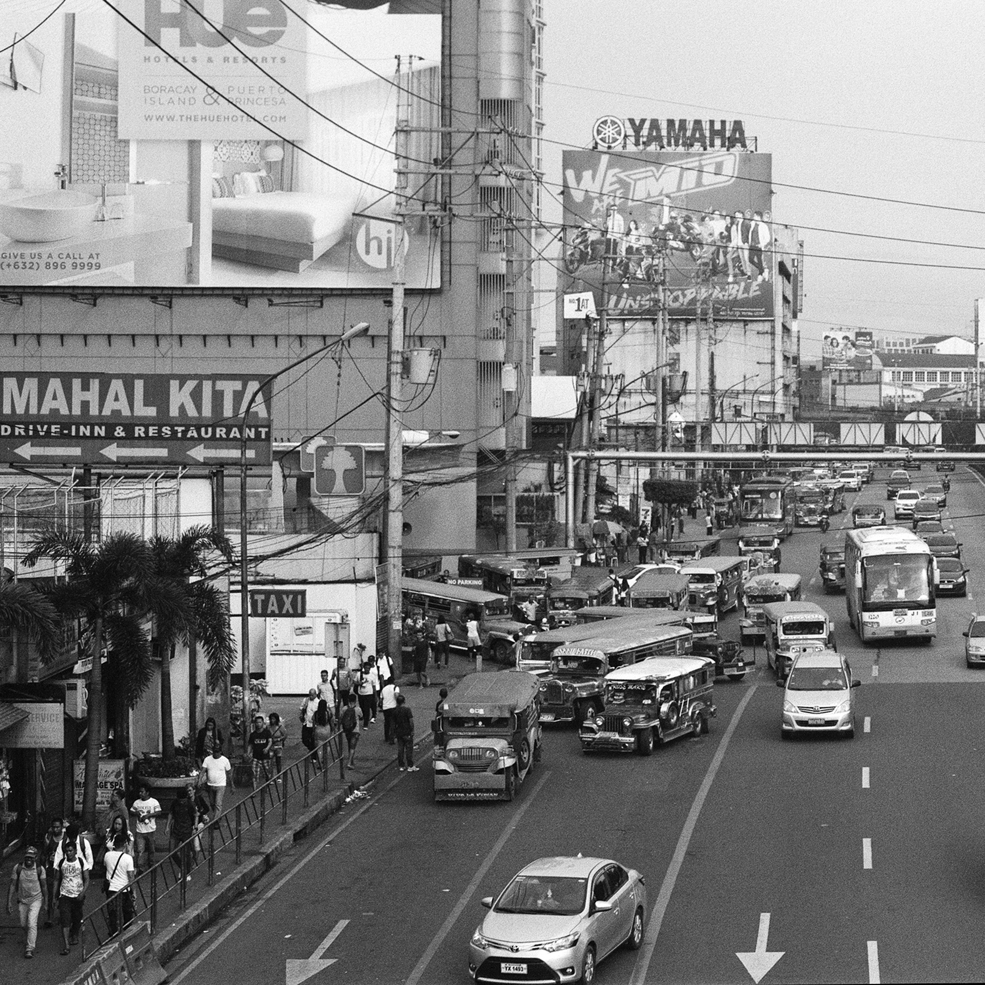 Black and white street-level view busy commercial street with buses jeepneys and market activity