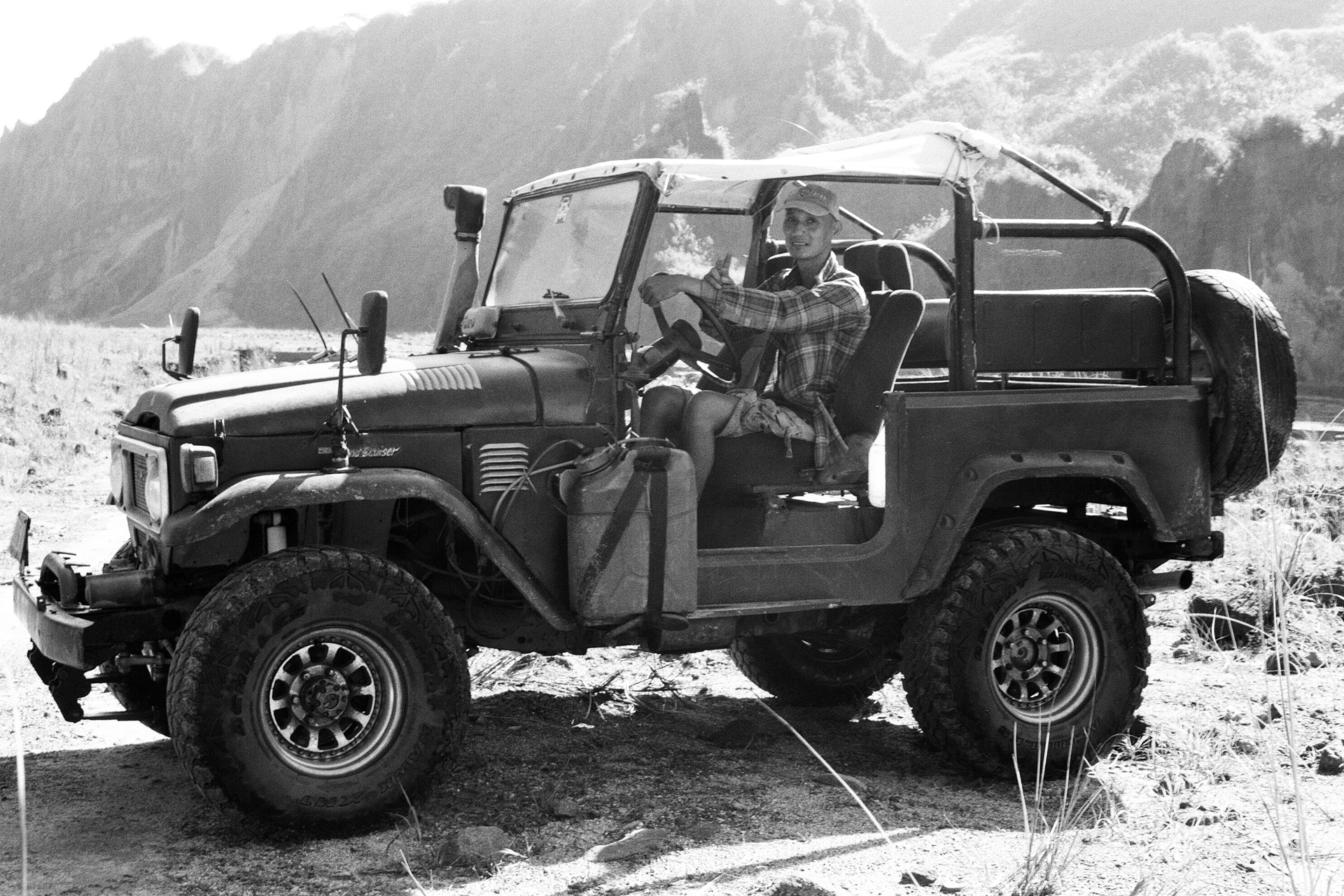 Black and white man sitting in open jeep vehicle in mountainous landscape