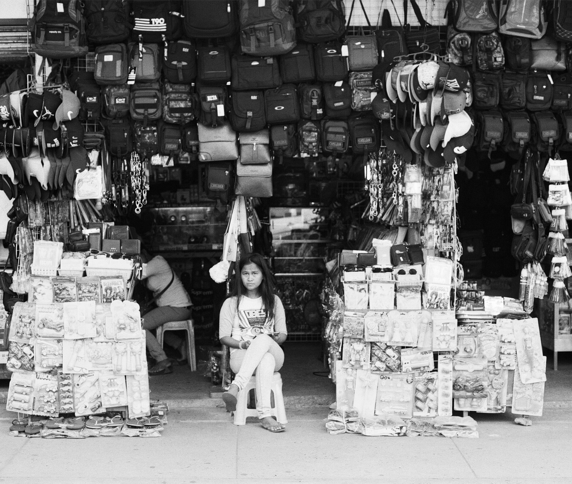 Black and white woman vendor sitting in market stall surrounded by merchandise and goods