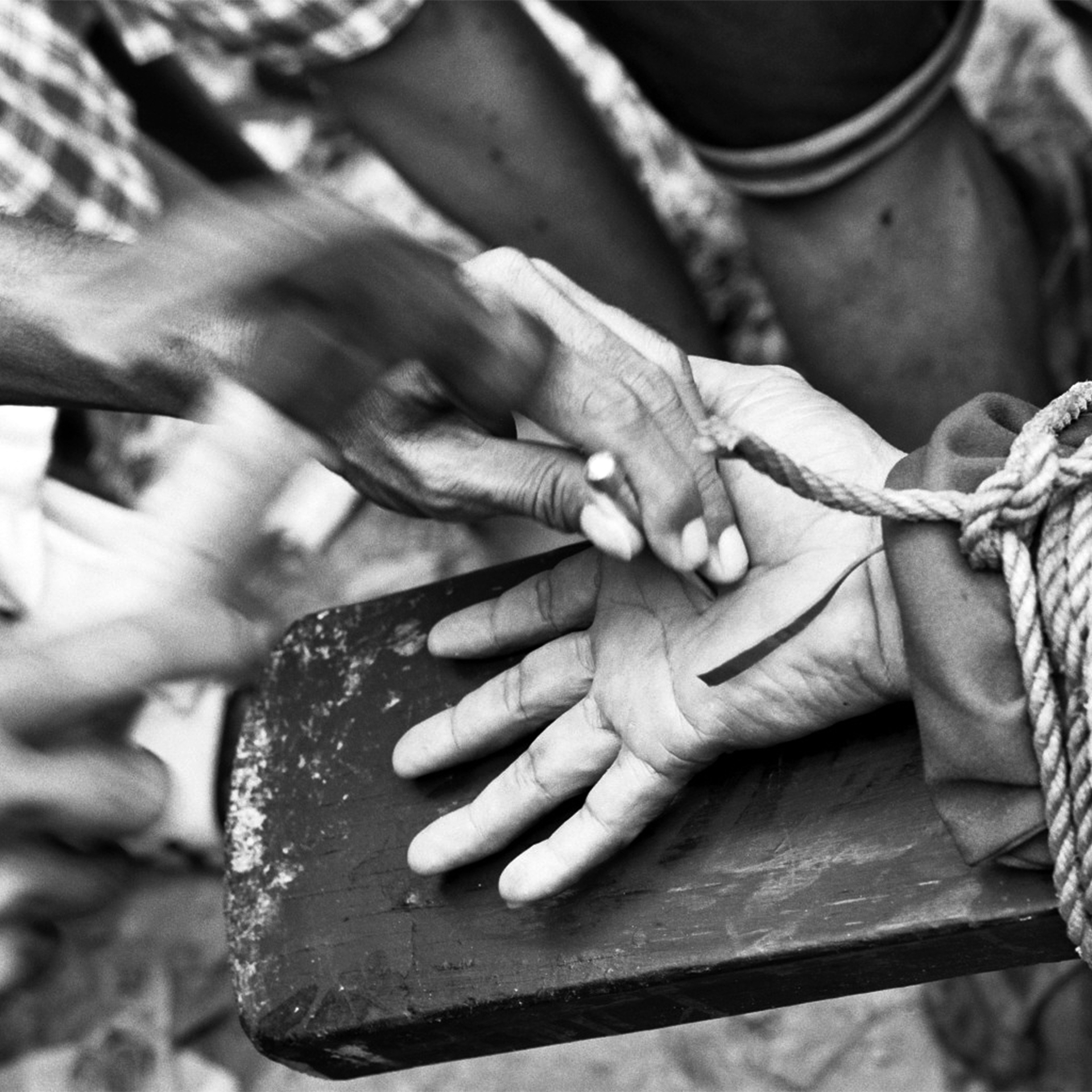 Black and white close-up of hands working with knife and rope in traditional craft