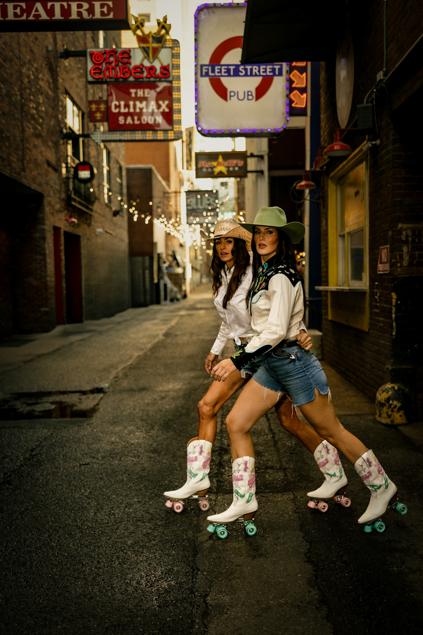 Two models skating through a neon-lit Nashville alley in cowboy hats and roller-skate boots