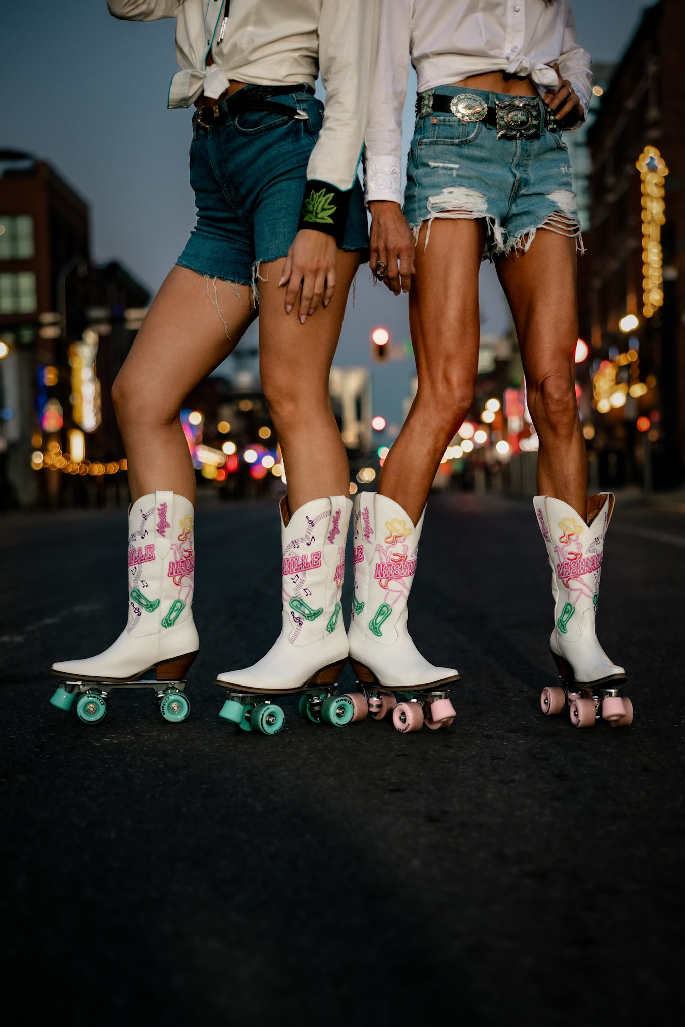 Close-up of embroidered neon-Nashville cowboy boots on roller skates standing in the middle of Broadway at dusk
