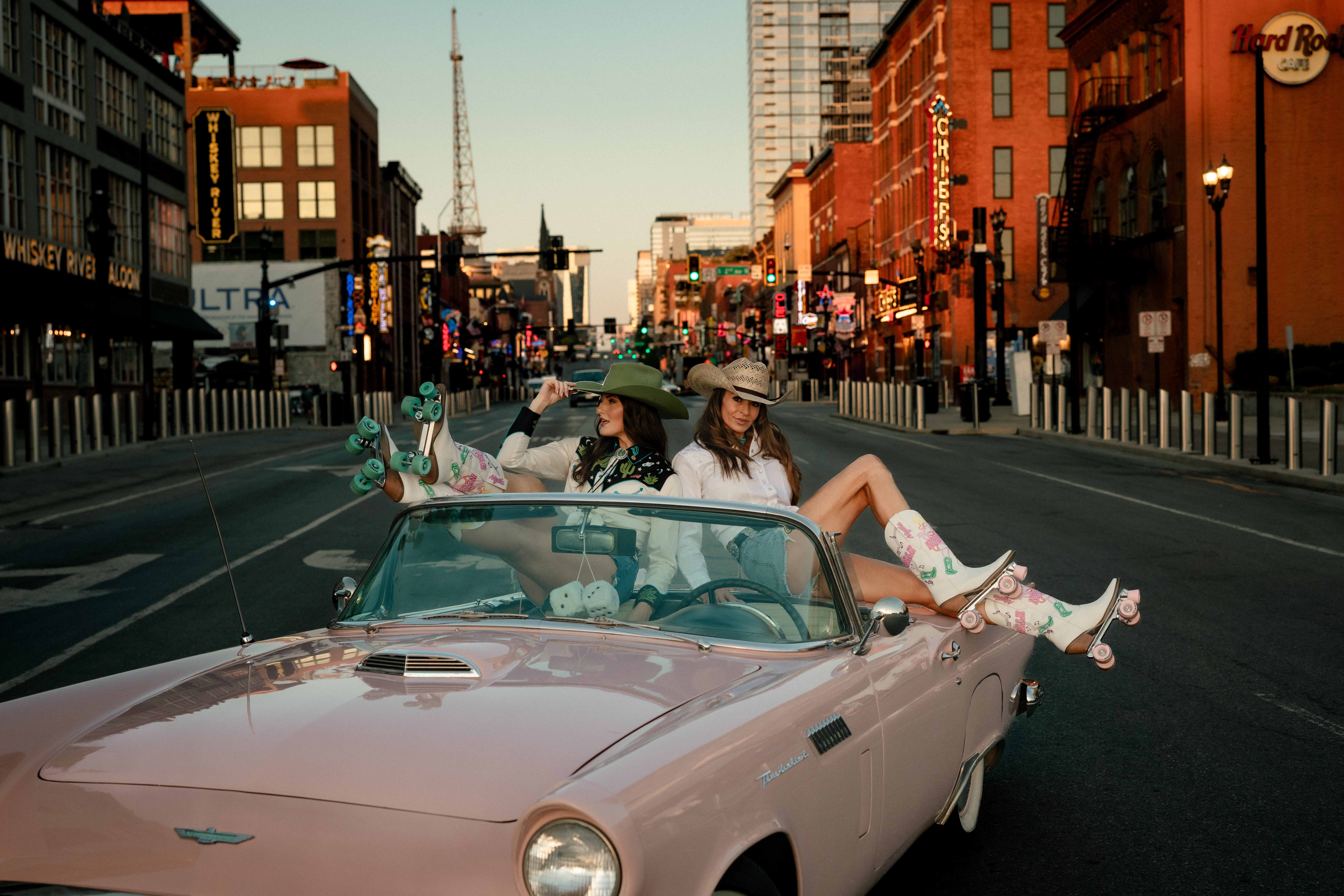 Pink vintage Thunderbird convertible parked on Broadway in downtown Nashville with two models in Western wear and roller-skate boots