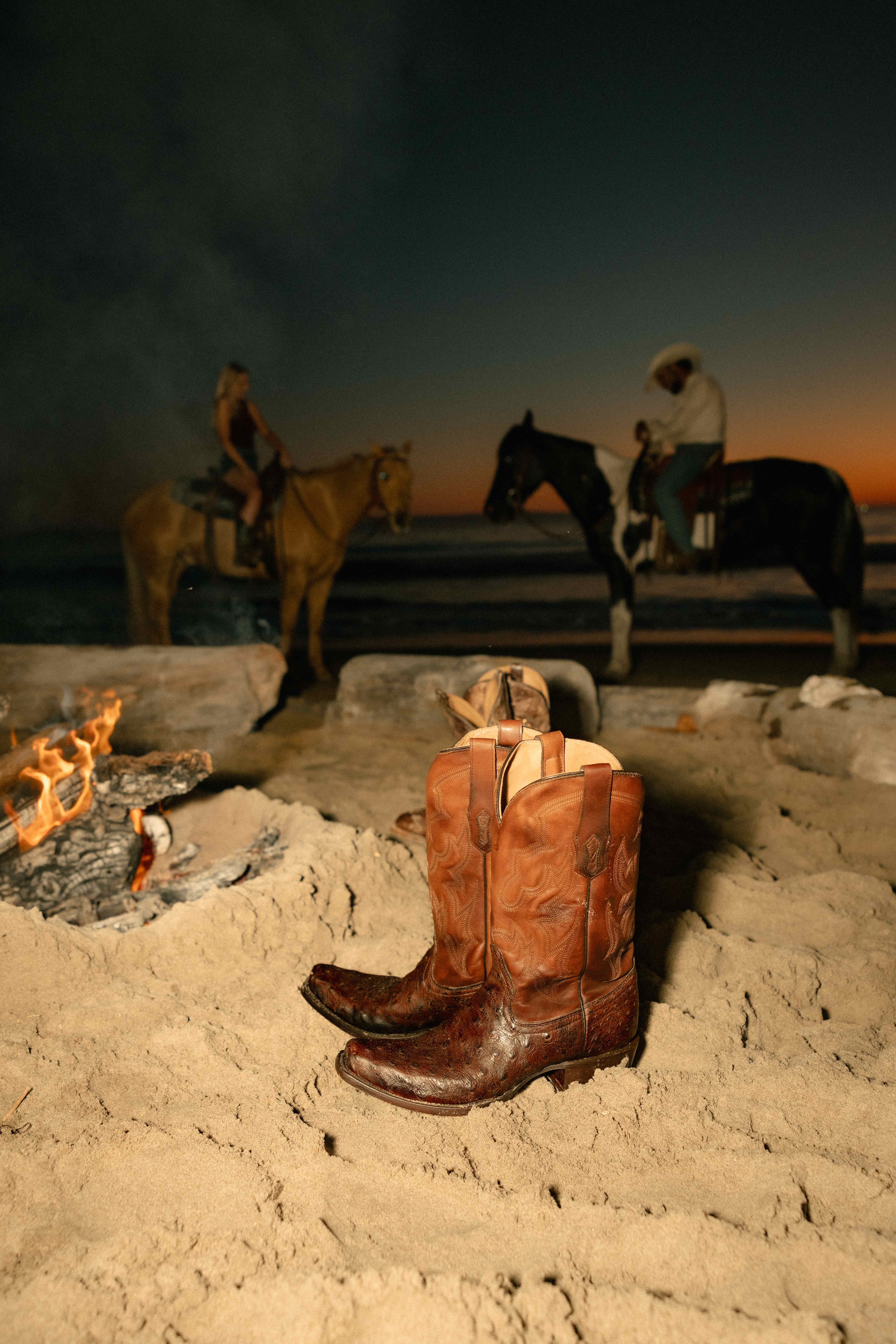 Cowboy boots by campfire with horses at dusk