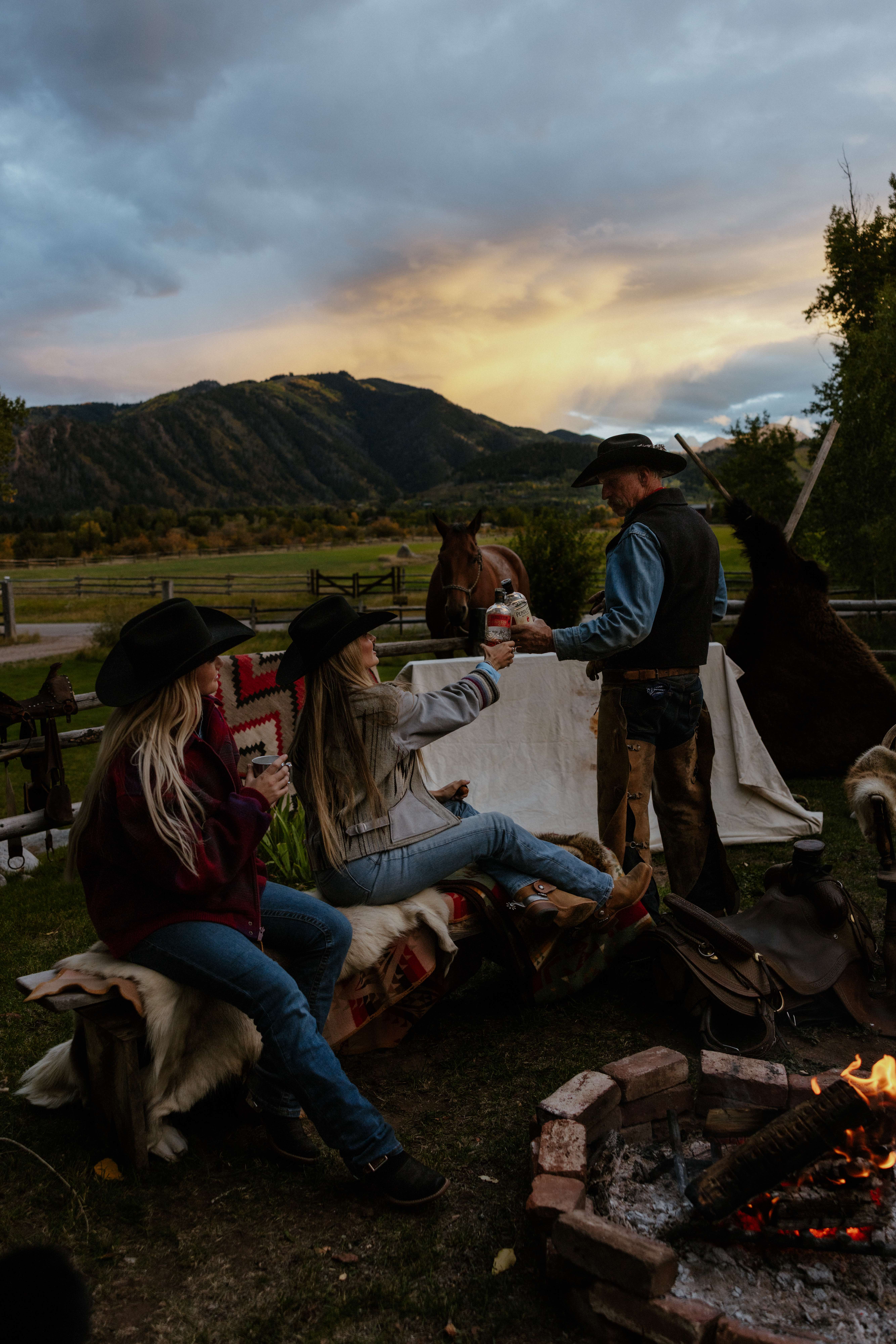 Cowboys gathered around campfire at sunset with mountains