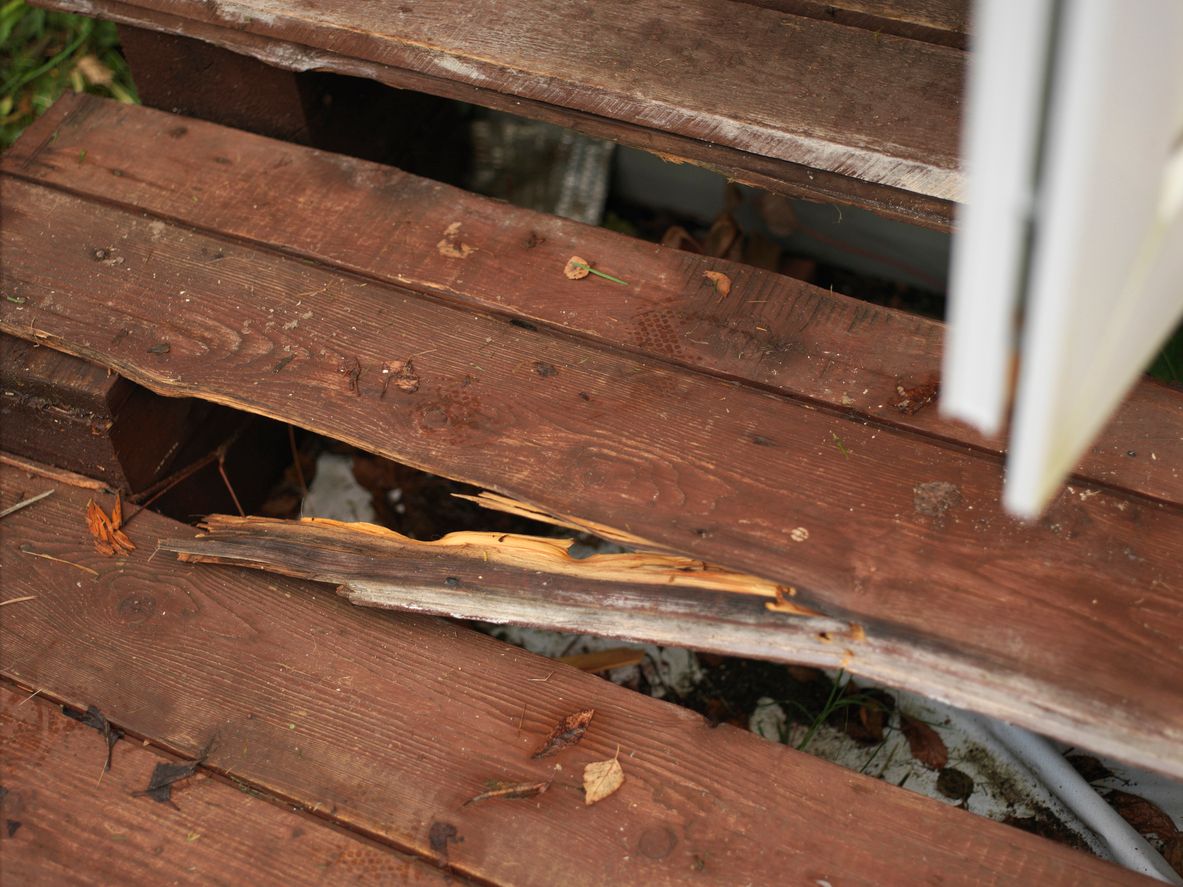 Close-up of weathered, splintered, and rotting reddish-brown wood deck boards in need of repair