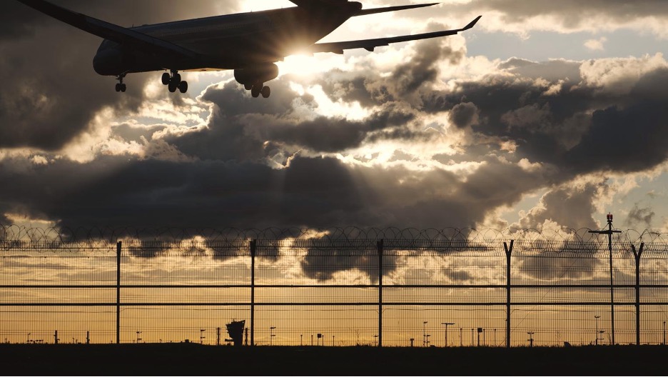 A commercial airliner silhouetted against a dramatic sunset sky on final approach.