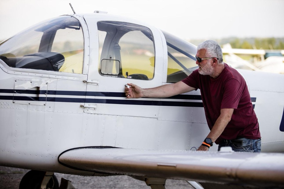 An older pilot pre-flighting his small aircraft on a quiet ramp.