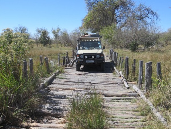 4x4 Land Cruiser crossing a rustic wooden log bridge in the African bush