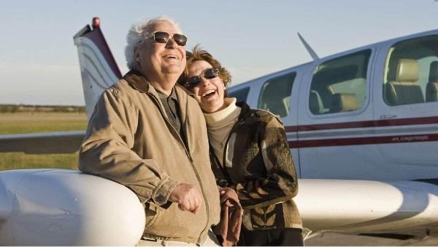 An older couple laughing together in front of their airplane after a flight.