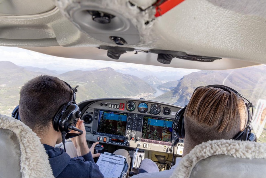 Two student pilots flying a glass-cockpit aircraft over mountainous terrain during a training flight.