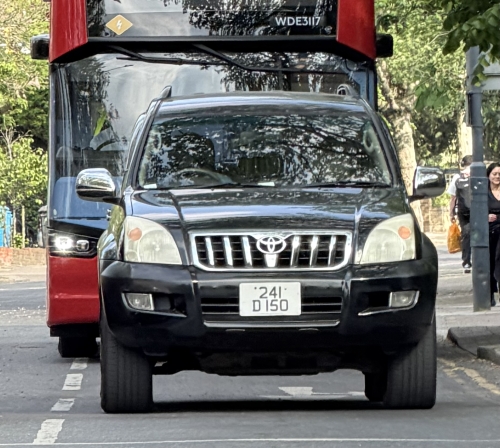 Plaque diplomatique britannique jaune 241 D 150 sur un Toyota Land Cruiser noir circulant à Londres devant un bus rouge à impériale — code 241 correspondant au Sénégal, statut D (agent diplomatique)