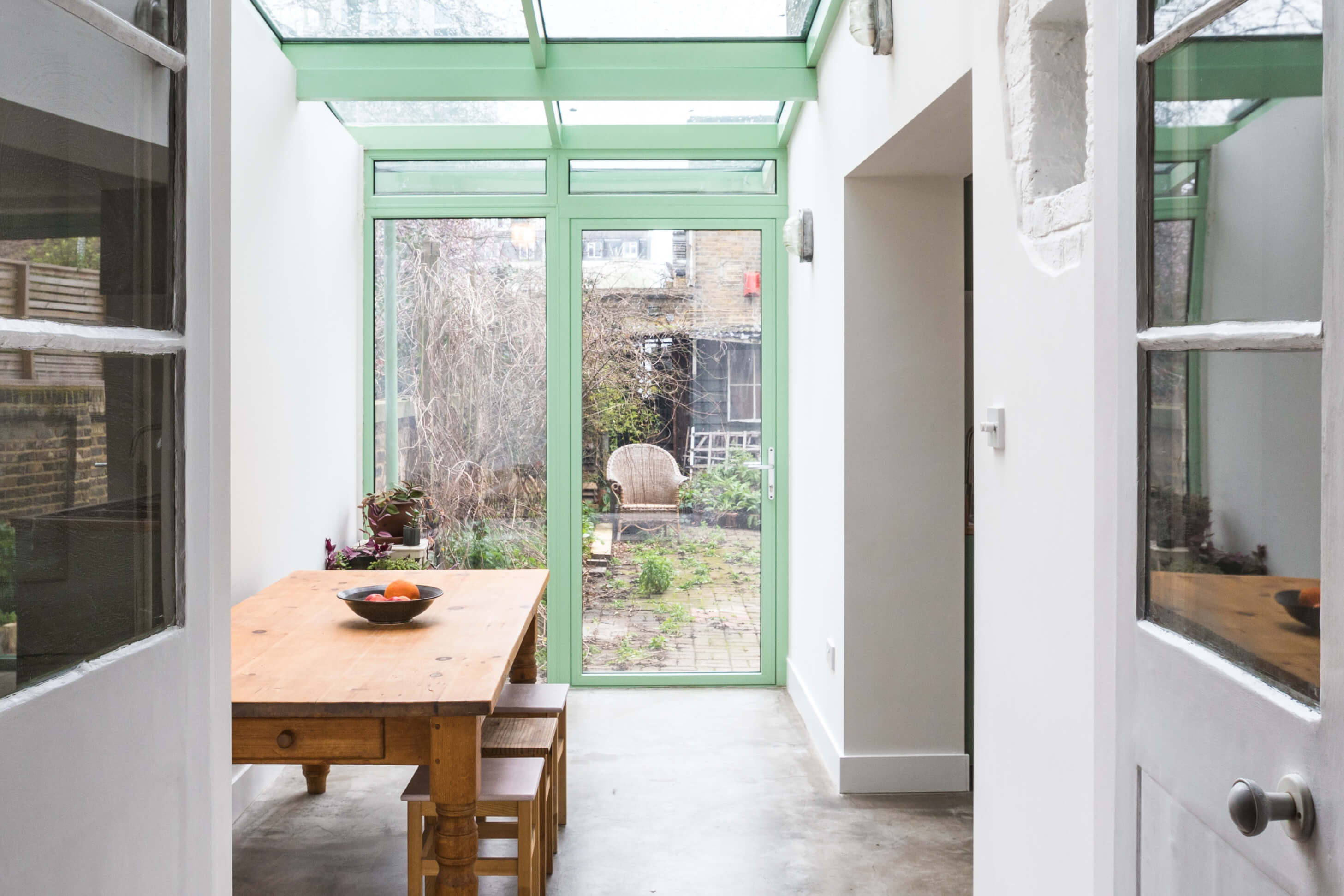 Bright conservatory dining space with mint green framed windows and doors, featuring a rustic wooden table