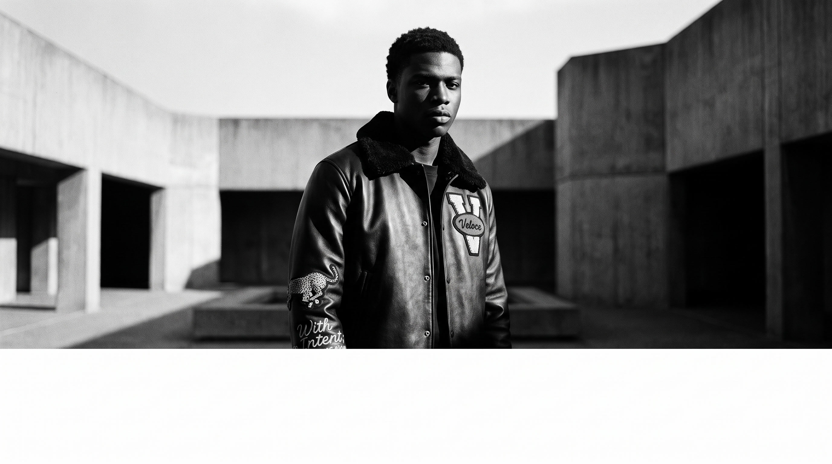 Black model wearing the VELOCÉ varsity jacket in a concrete courtyard