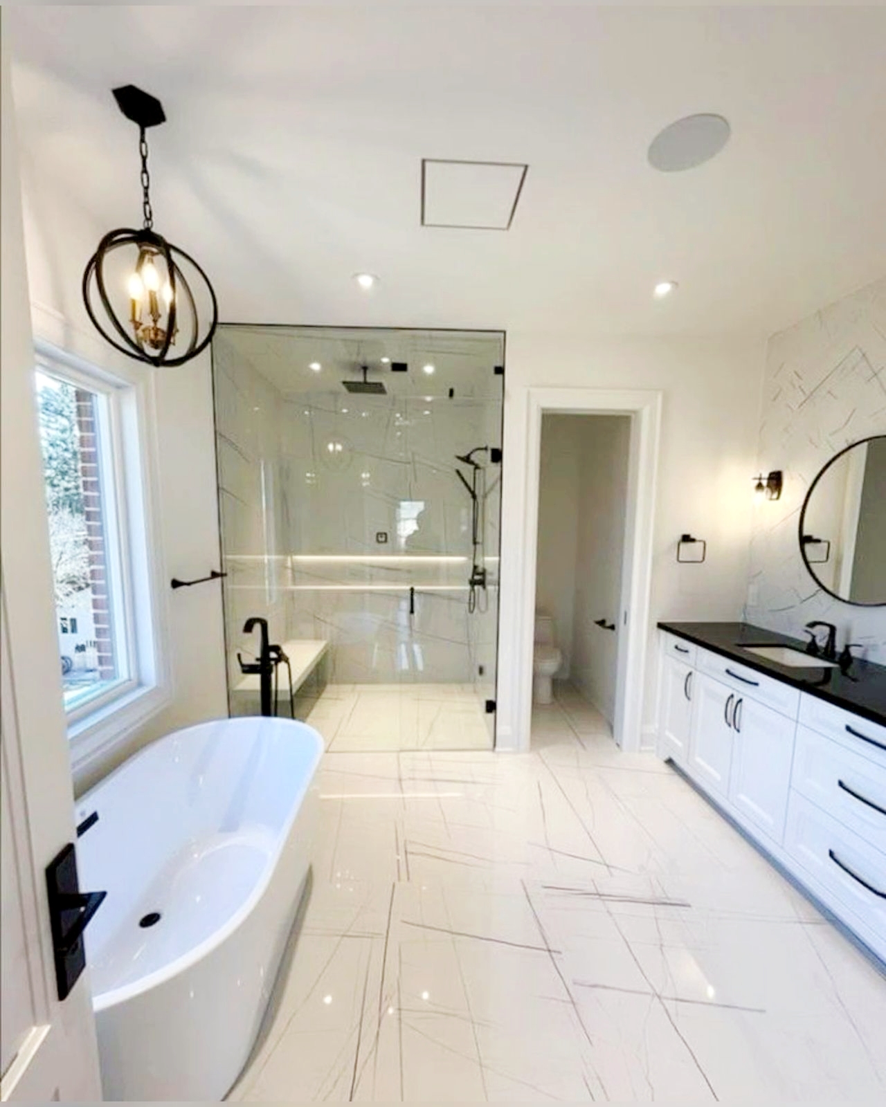 Contemporary white bathroom with frameless glass shower enclosure, black fixtures, integrated niches, freestanding tub