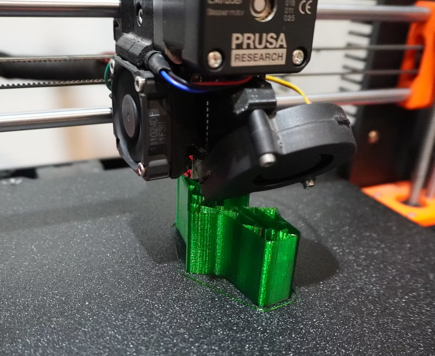 Close-up of a Prusa printer head printing the first layers of a green workshop jig on the build plate