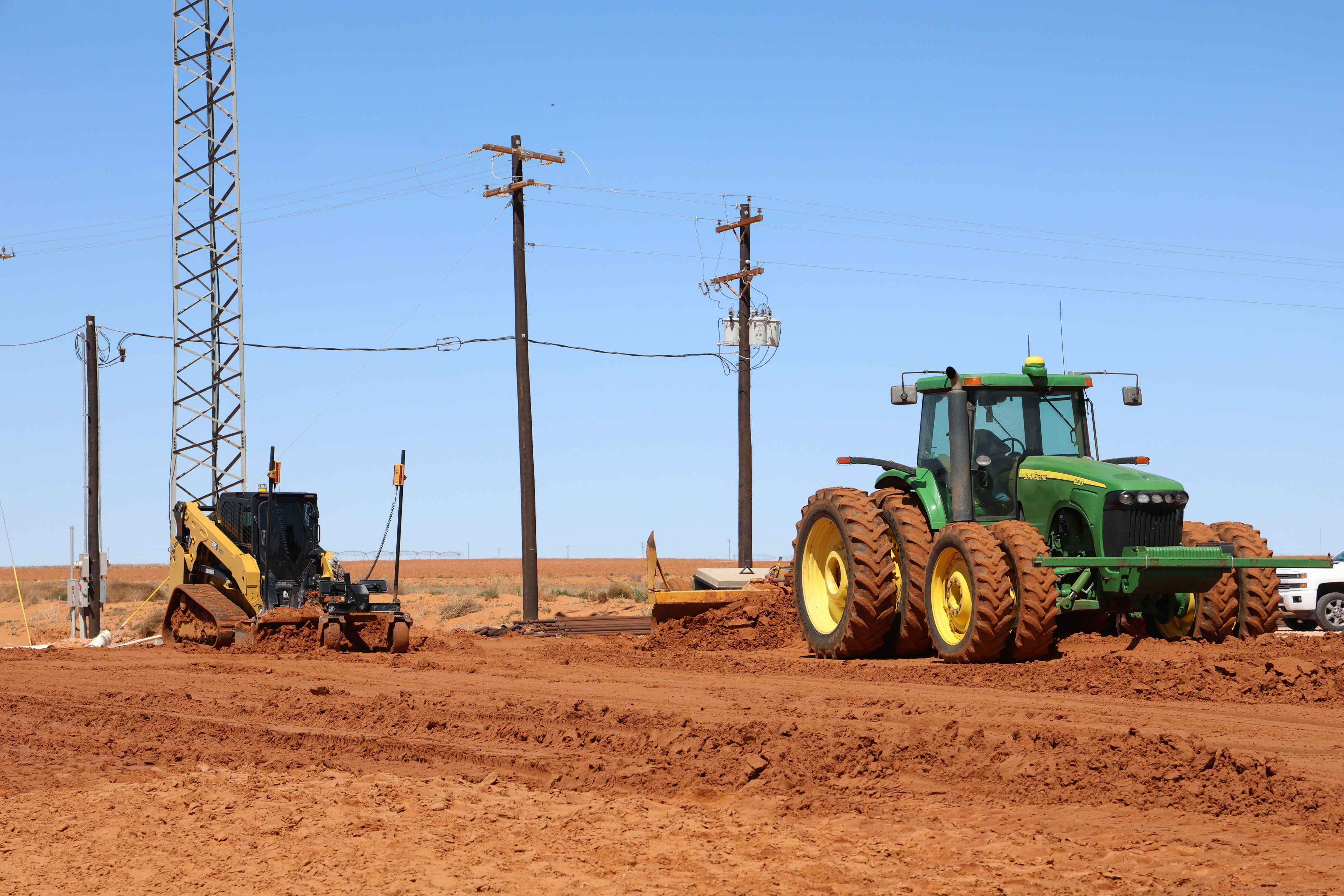 Heavy equipment including tractor and skid steer preparing access roads across West Texas landscape