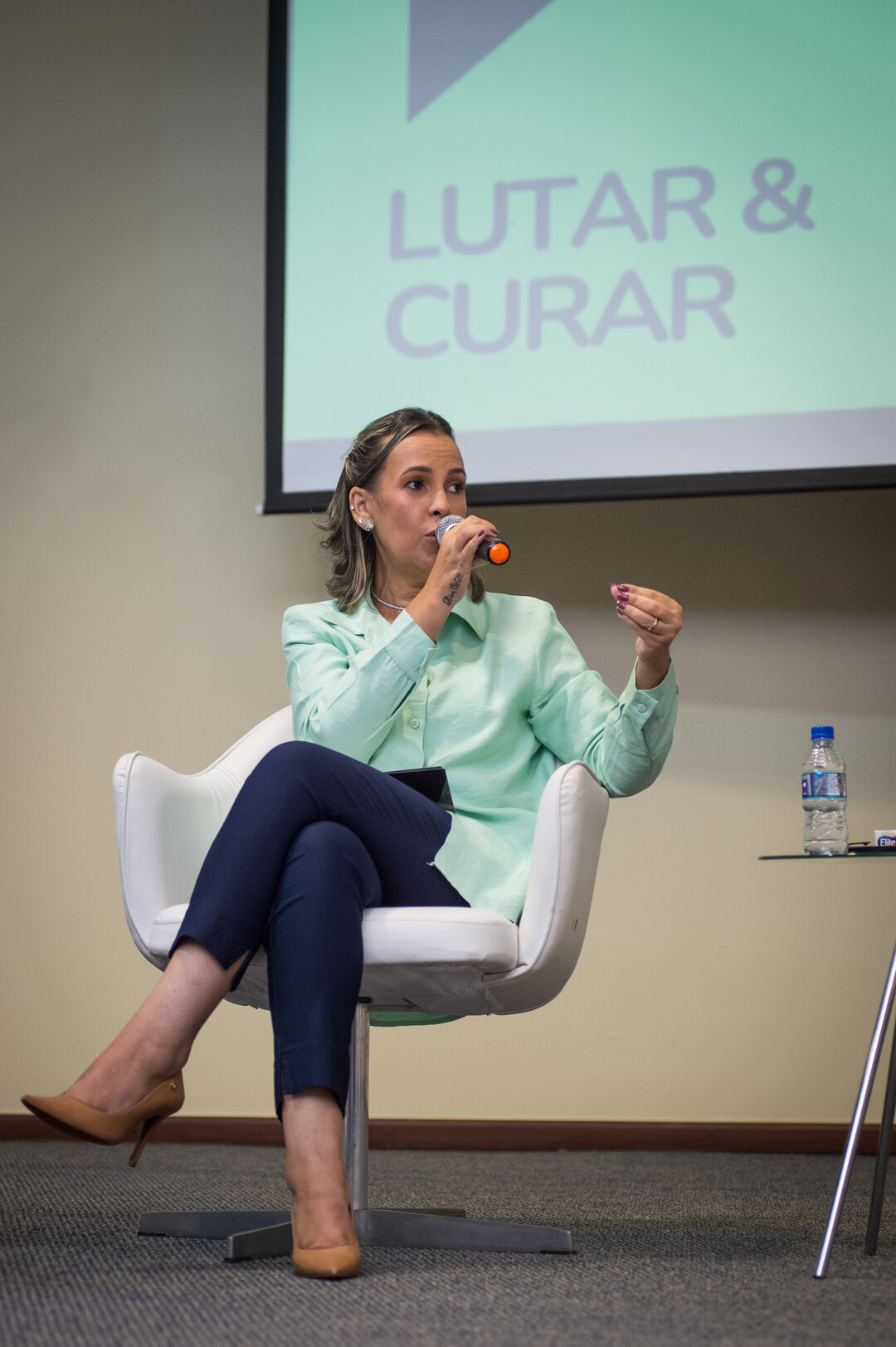 Mulher em camisa verde com gestos expressivos ao microfone