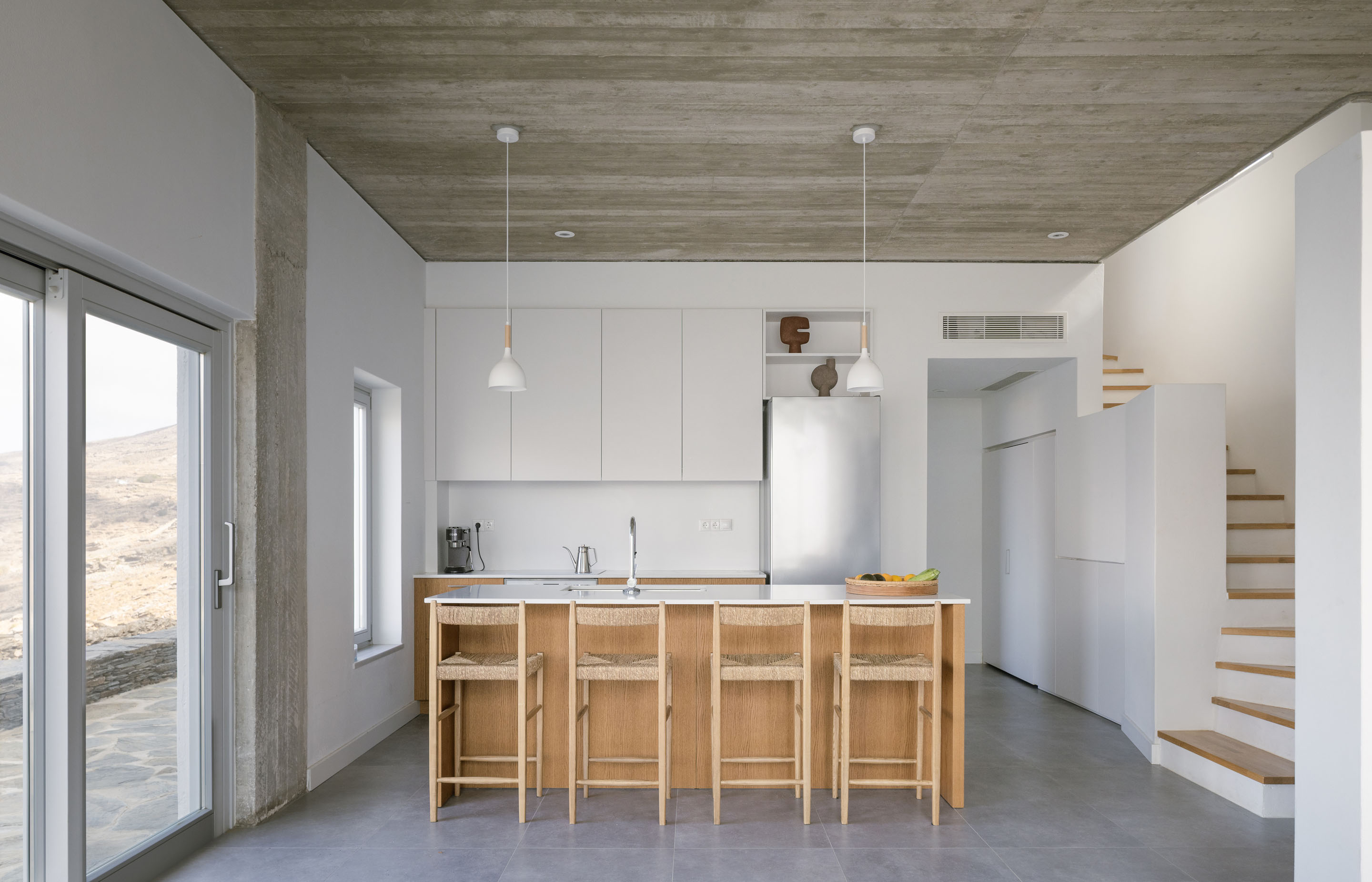 Open kitchen with concrete ceiling, white cabinetry and an oak island with woven bar stools