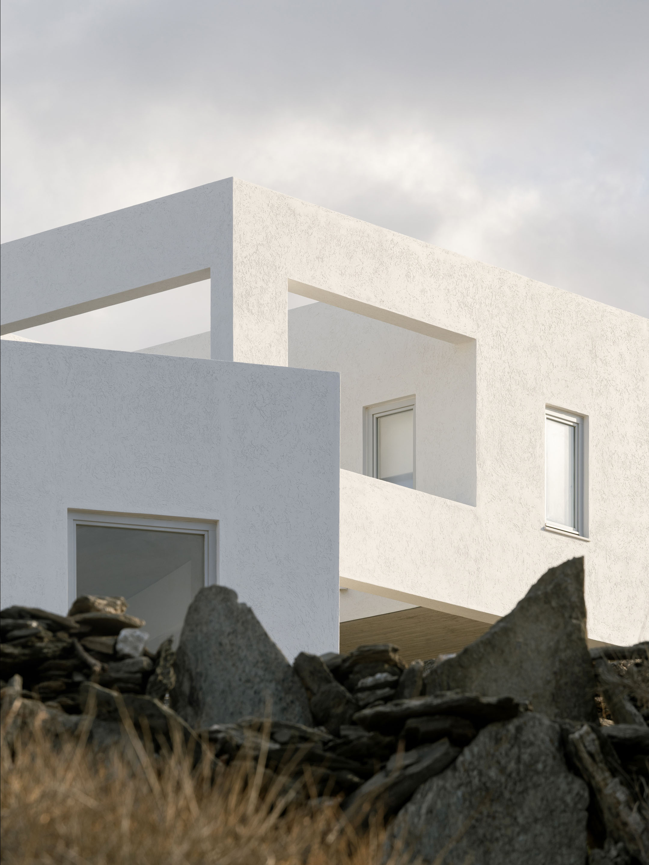 White cubic architecture of Korthi Houses against dramatic sky and stone walls