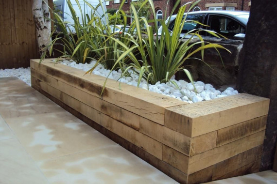 Modern raised planter bed made from railway sleepers with decorative stones and ornamental grasses