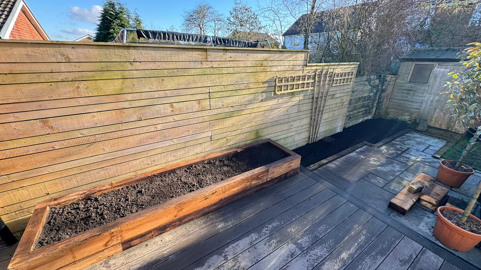 Garden renovation featuring railway sleeper raised bed with fresh soil and wooden decking