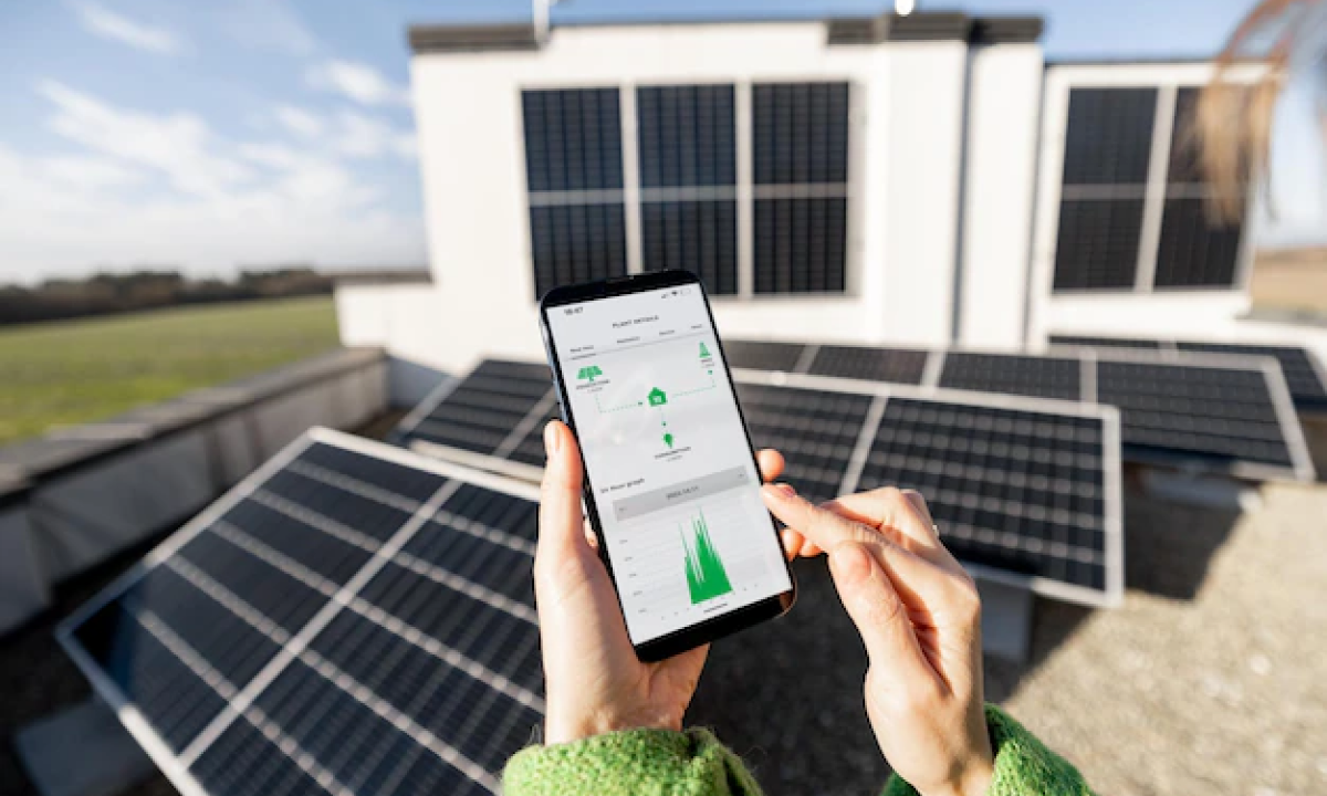 Mani che tengono smartphone con app di monitoraggio solare davanti a pannelli fotovoltaici