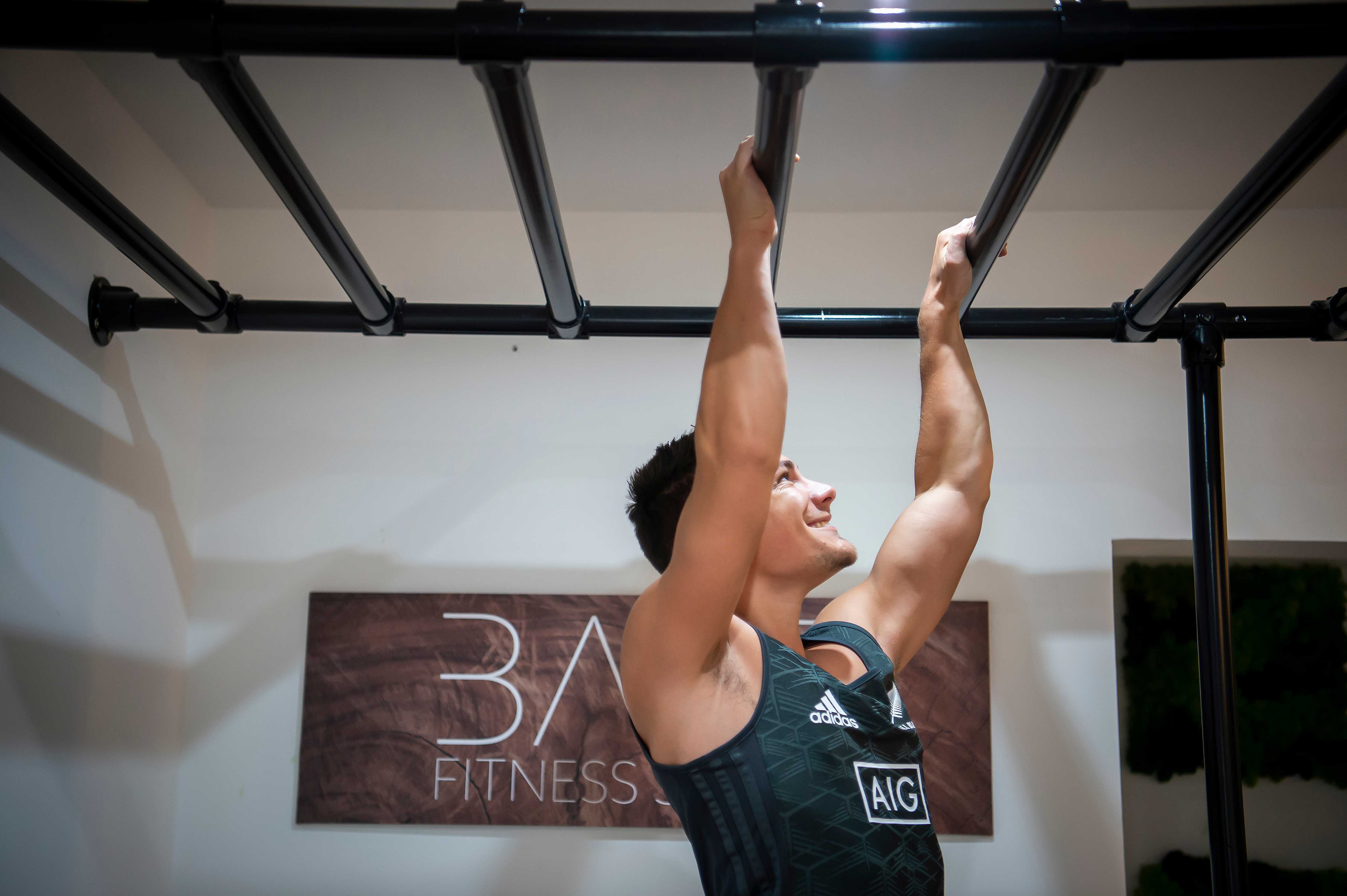 Pull-ups on monkey bars with Bare Fitness Studio sign