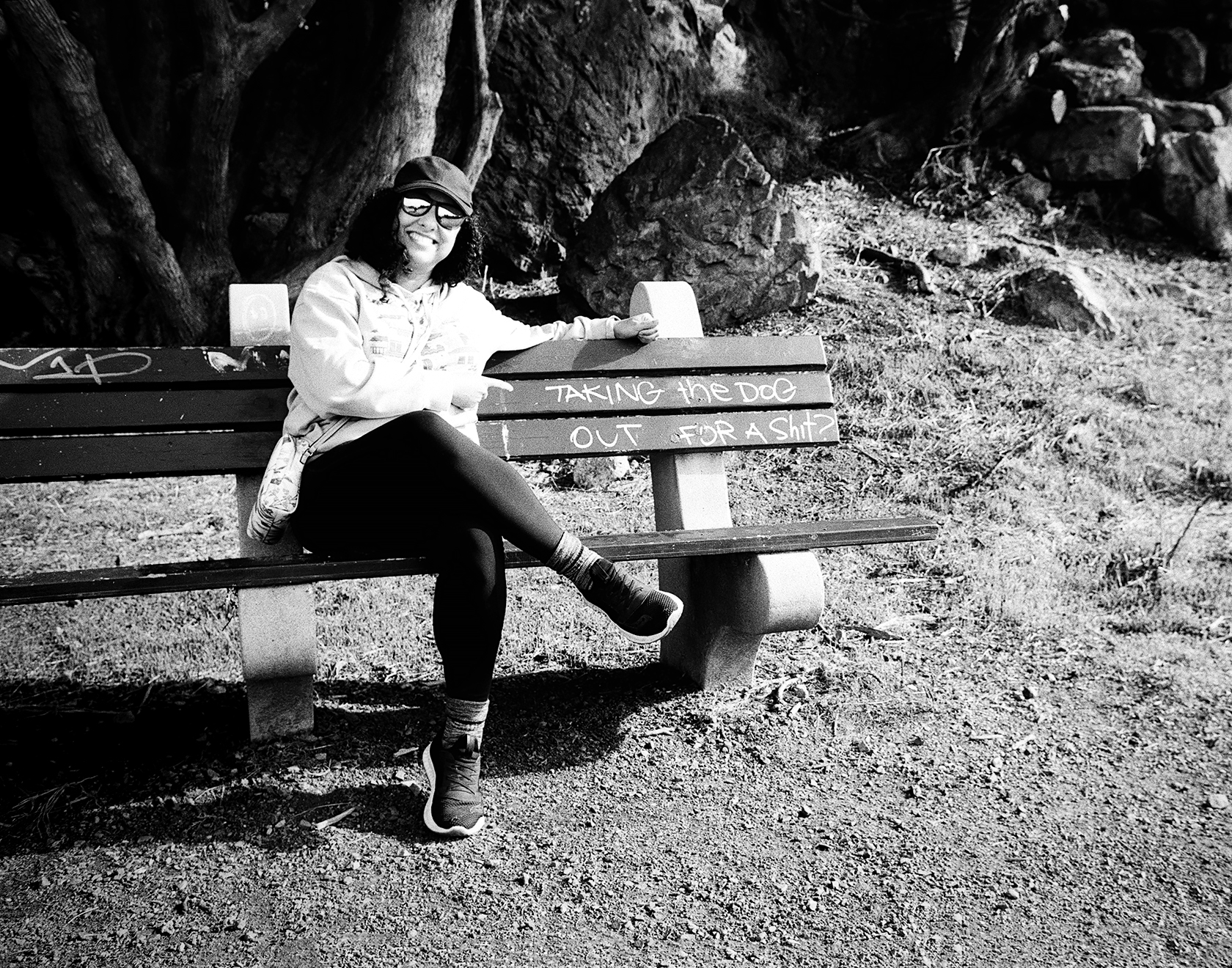 Humorous portrait of person posing confidently on bench with text reading Taking the dog out for a shit surrounded by large cypress trees in natural setting
