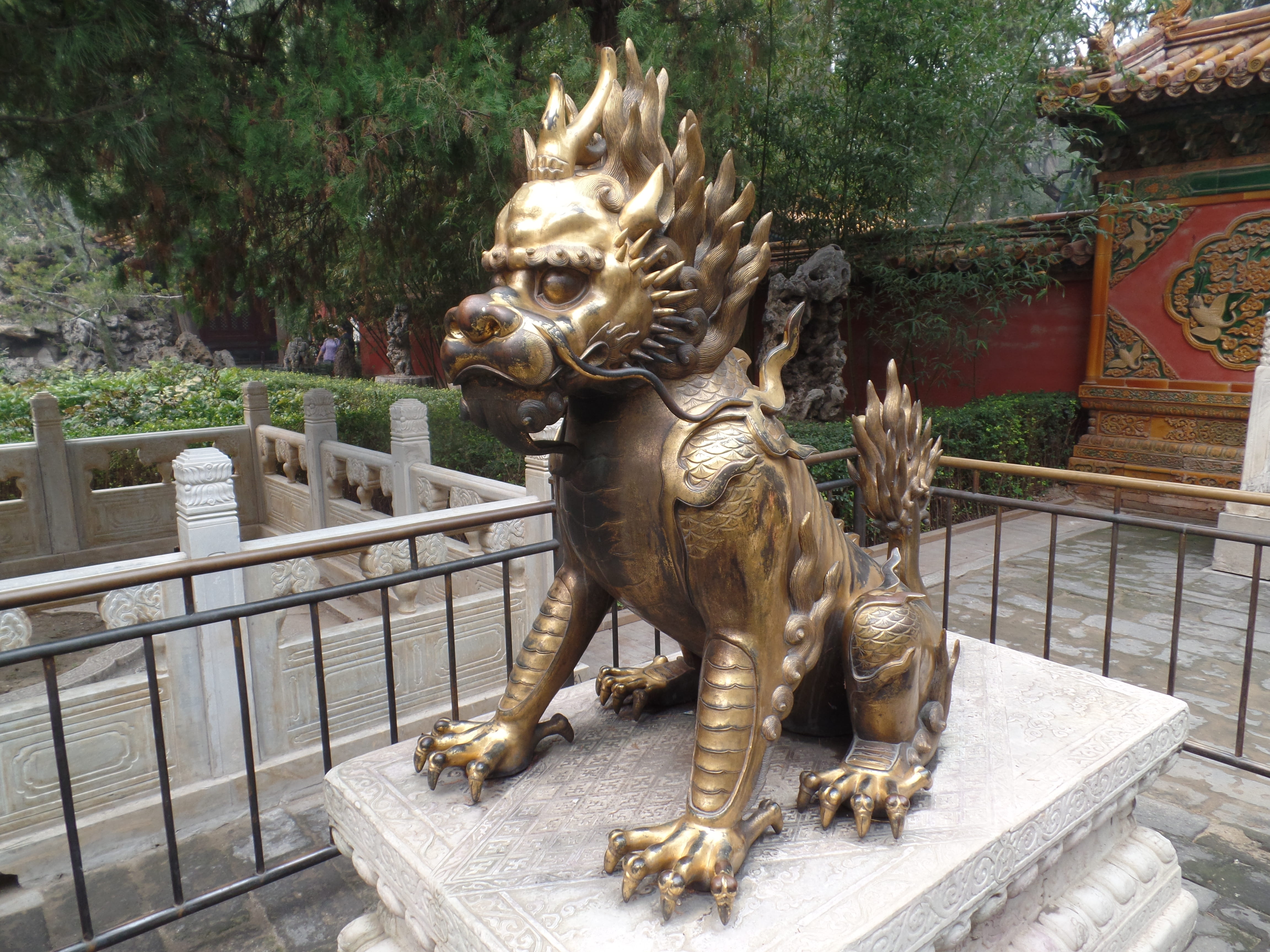 Close-up of ornate golden qilin guardian dragon statue on stone pedestal, rich detail and temple architecture