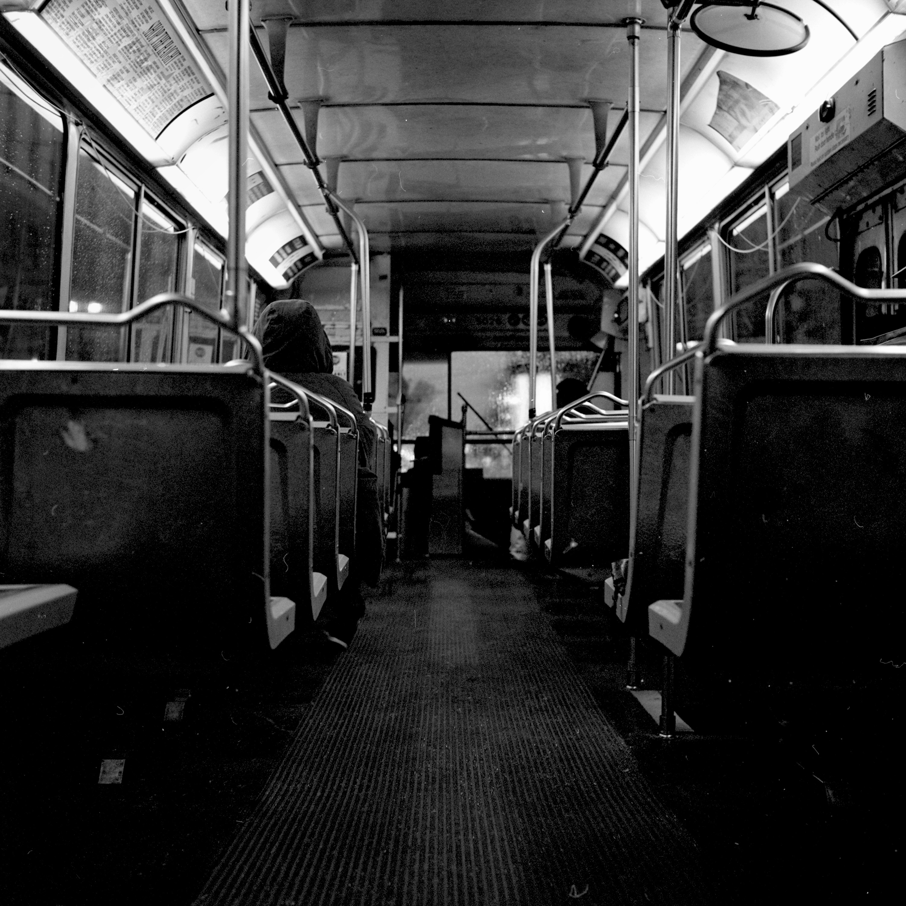 Empty bus or transit vehicle interior with rows of seats, metal handrails, and fluorescent ceiling lights
