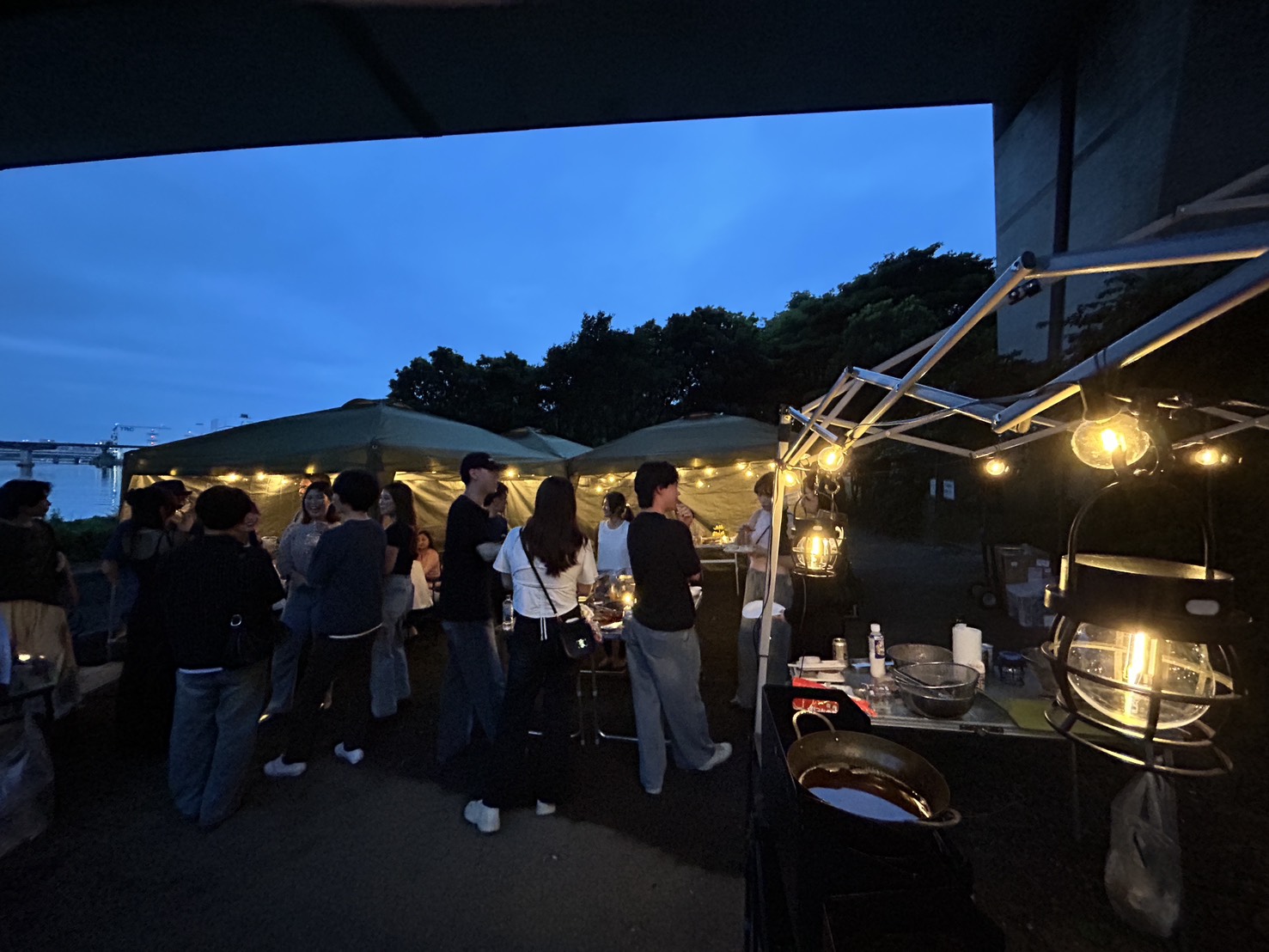 夕暮れの川辺でガーランドが灯るBBQ交流会の様子