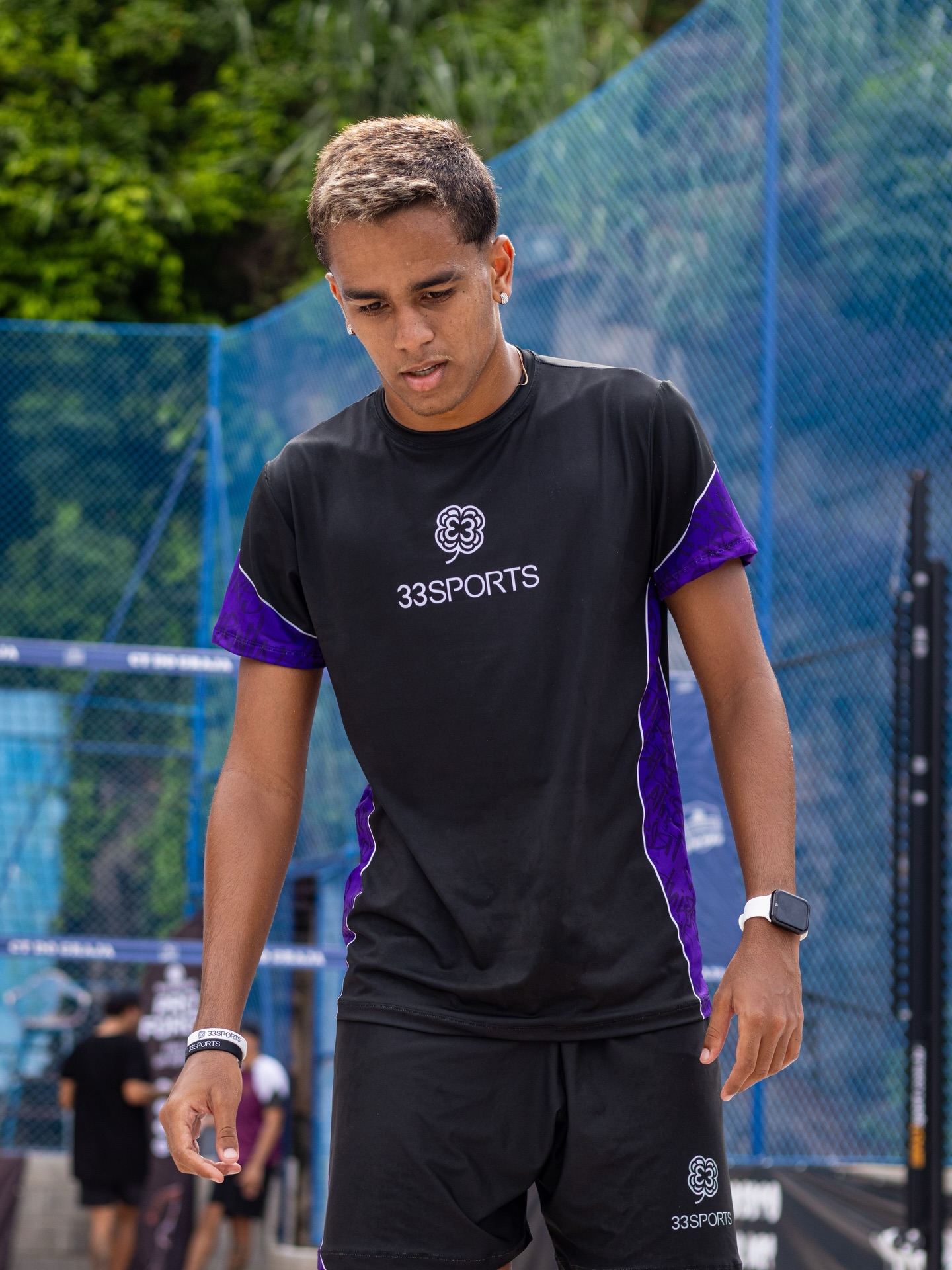 Atleta masculino caminhando com uniforme preto e detalhes roxos 33Sports em quadra com tela azul