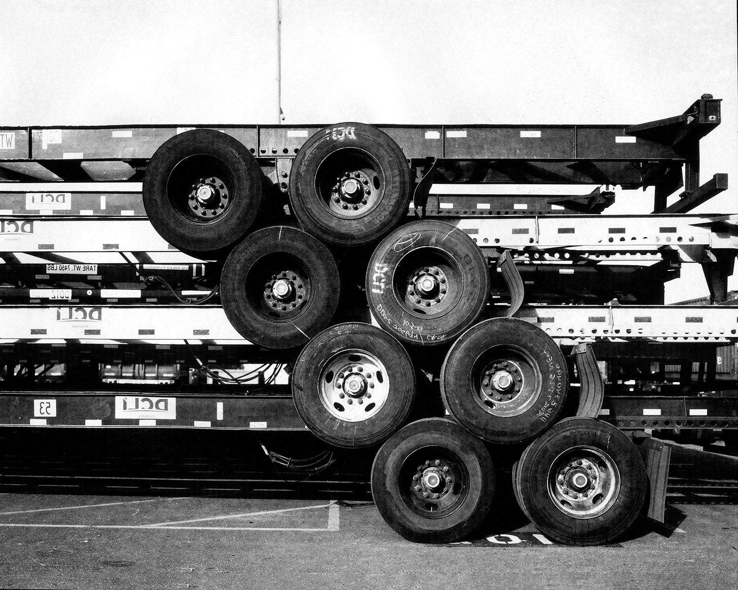 Geometric stack of large truck tires arranged in pyramid formation against industrial striped trailers