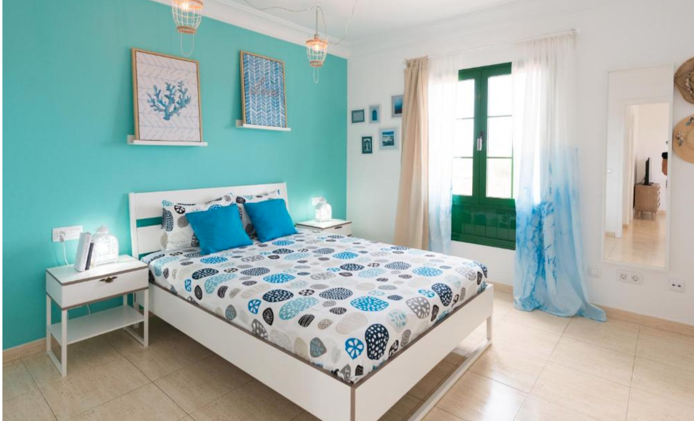 Turquoise bedroom with double bed, coral artwork, and green-framed window