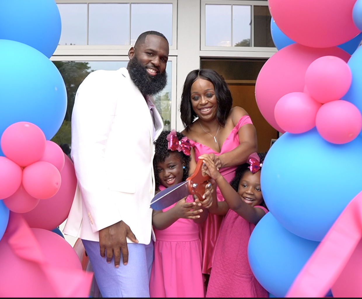 Andre Fluellen and family at a ribbon cutting ceremony with pink and blue balloons