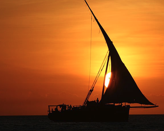 Traditional dhow sailboat silhouetted against beautiful orange sunset