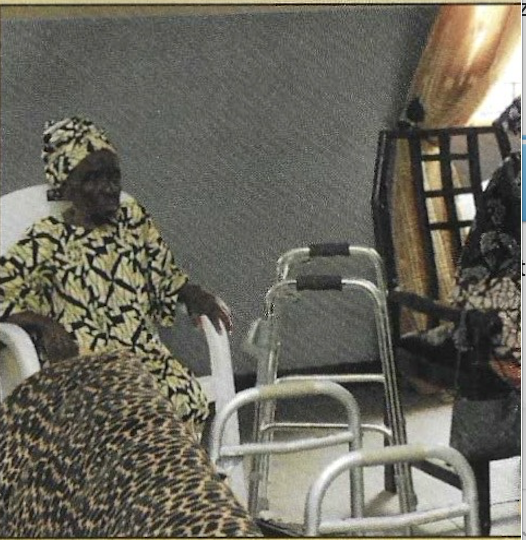 An elderly woman seated beside a donated walker